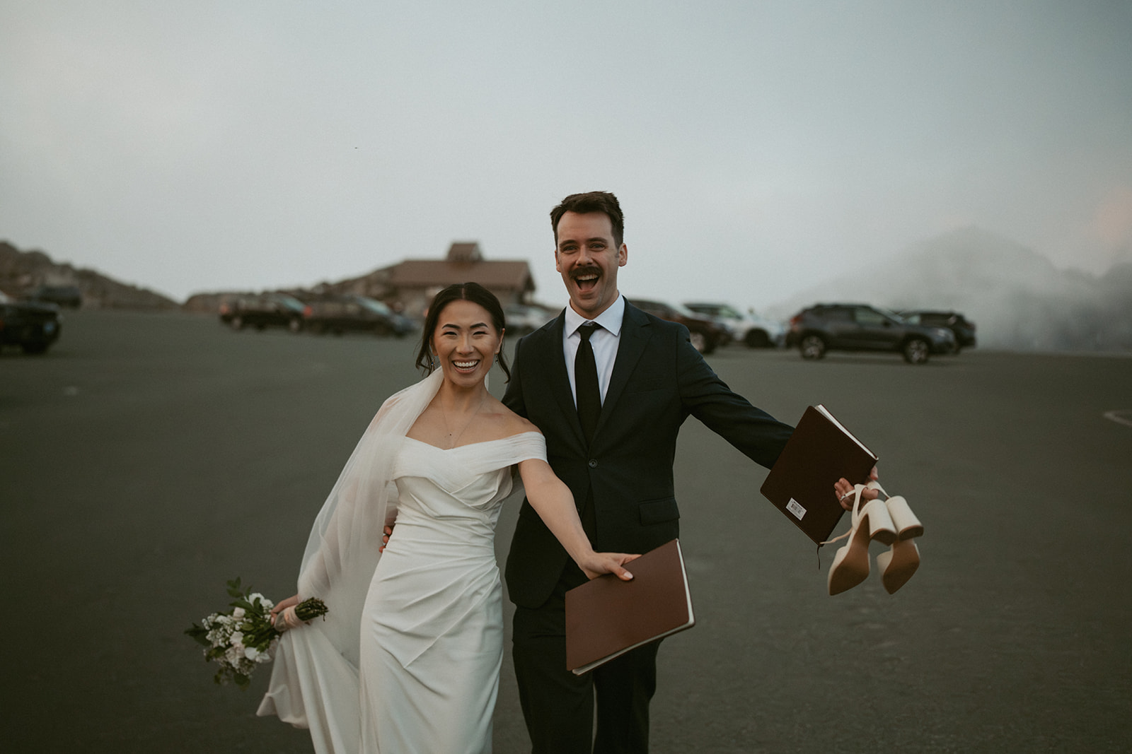 Just married, a joyful couple walks hand in hand with vows and shoes in hand at their Washington elopement.