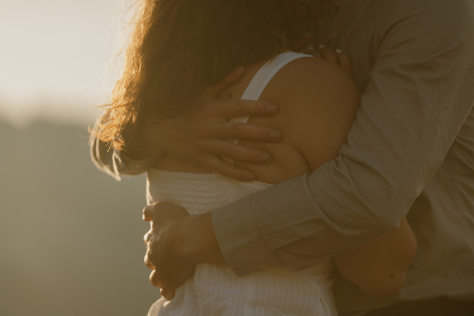 Close up of golden sun while man wraps arms around woman embracing her in a romantic moment during outdoor engagement photos