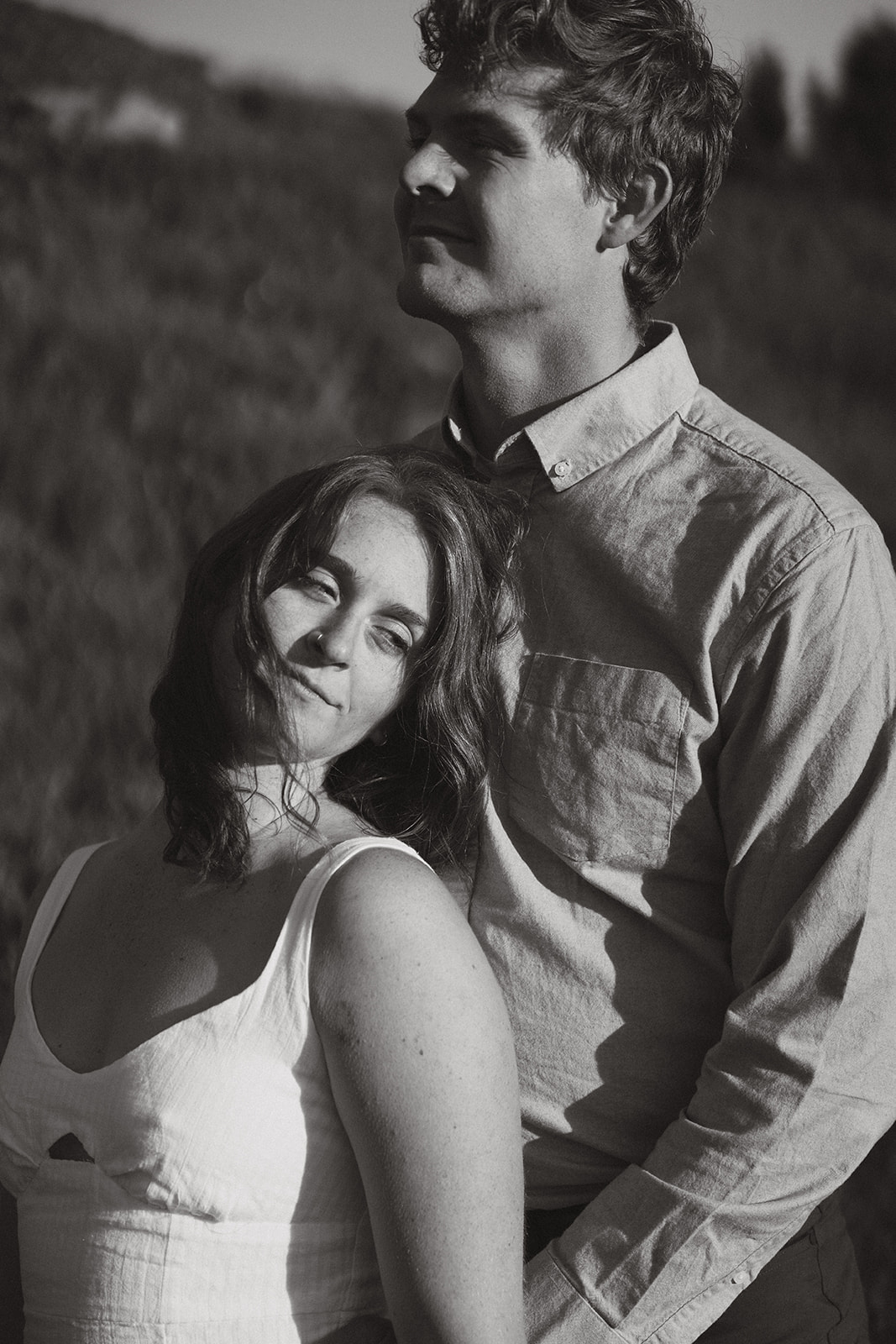 Black-and-white portrait of a couple sharing a quiet moment together, with soft expressions and the breeze lifting her hair.