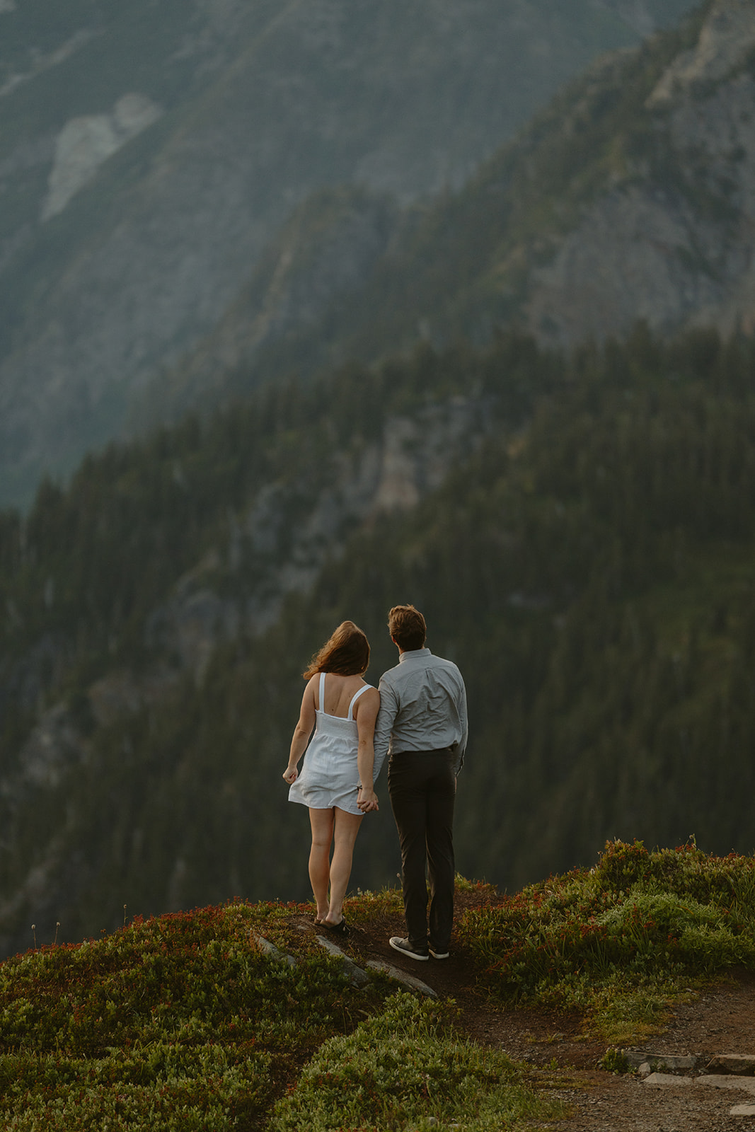 Newly engaged couple looking at mountain view while holding hands during outdoor engagement photos