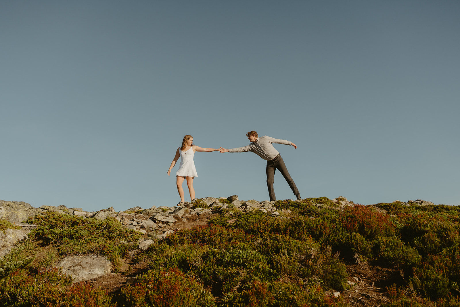 Man reaching for woman's hand across top of hill during outdoor engagement photos