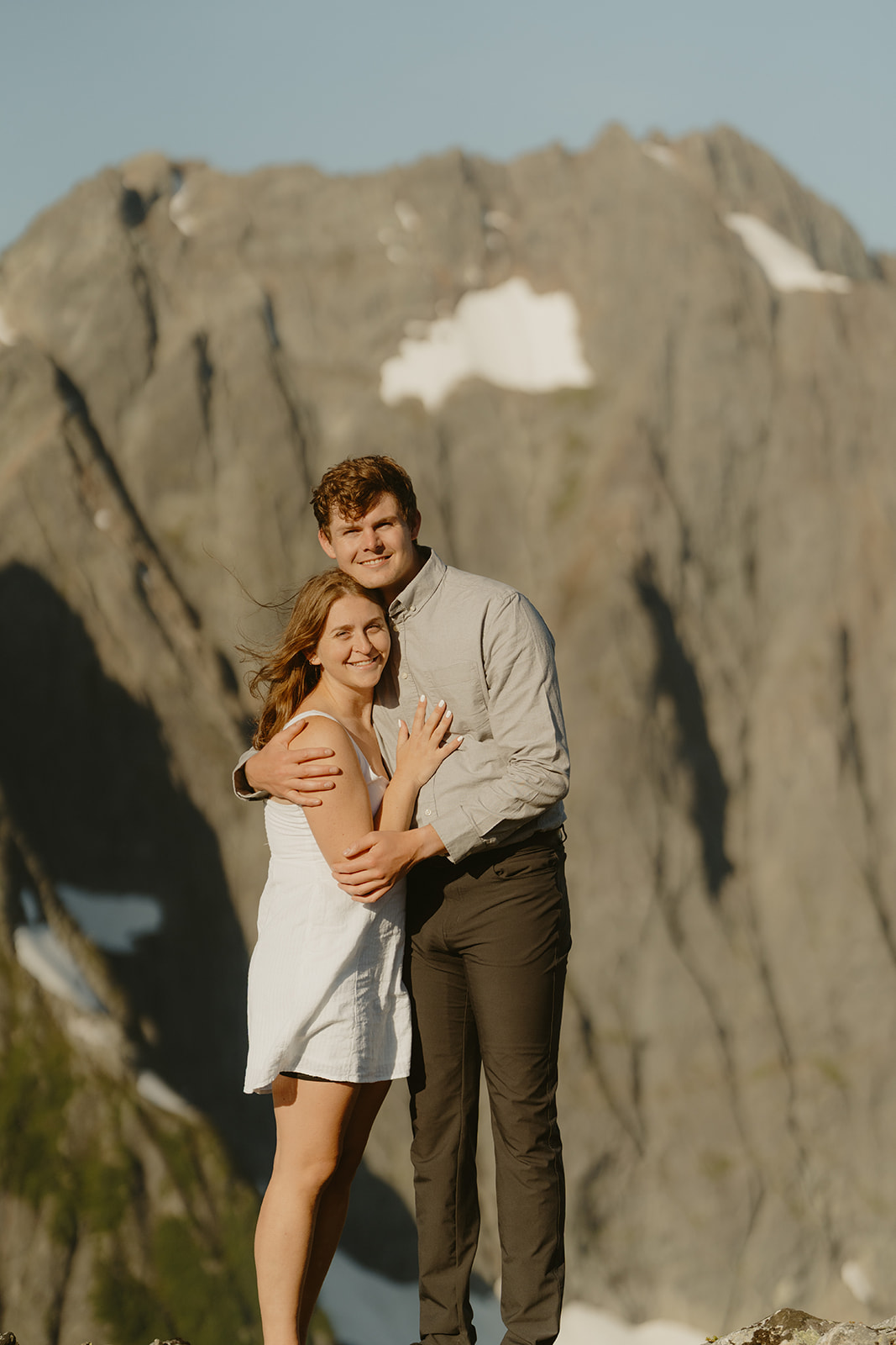 Man holds woman while she places her hand on his chest to showcase gold engagement ring