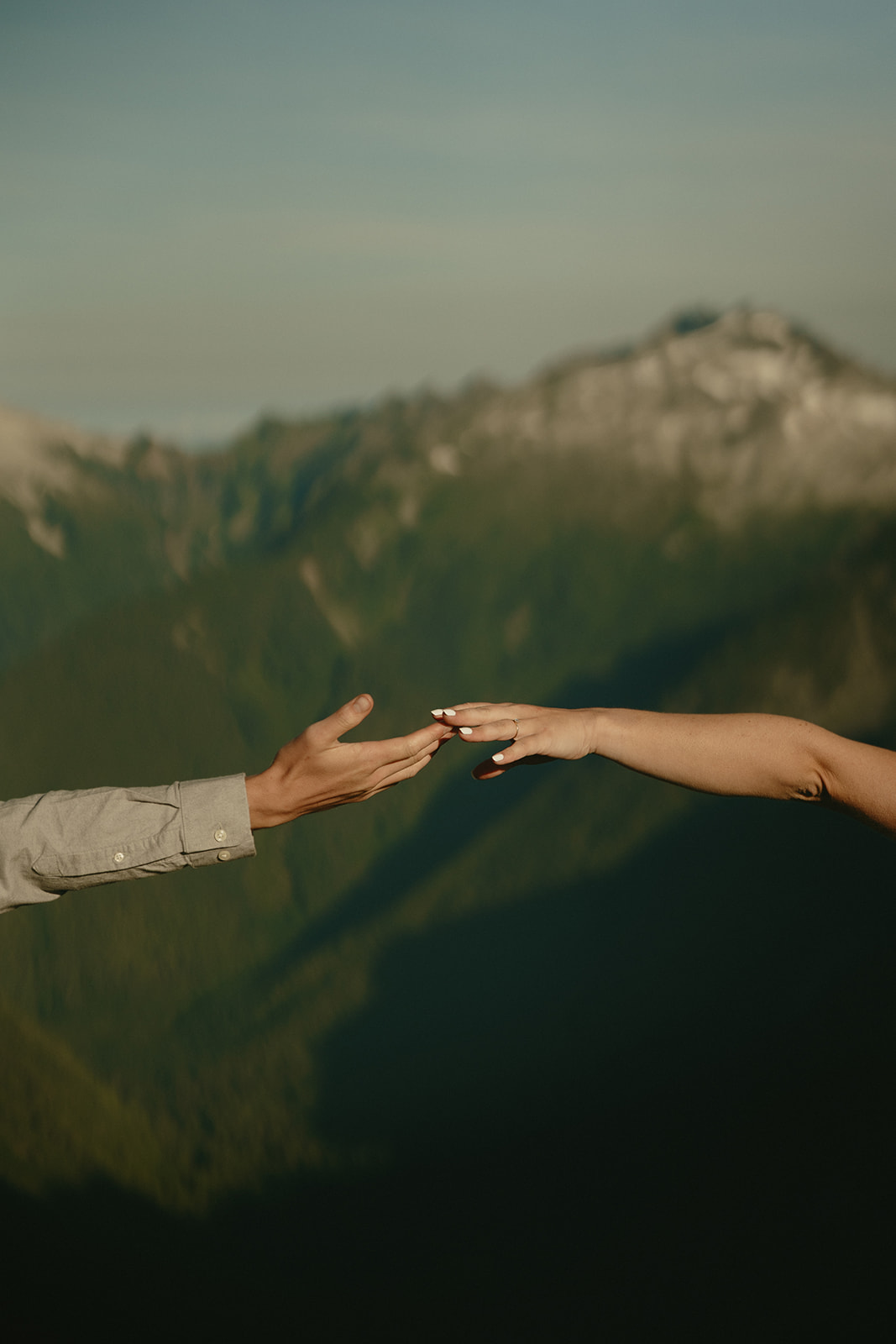 Close up of man and woman's hand reaching for one another with breathtaking washington landscape behind them during outdoor engagement photos