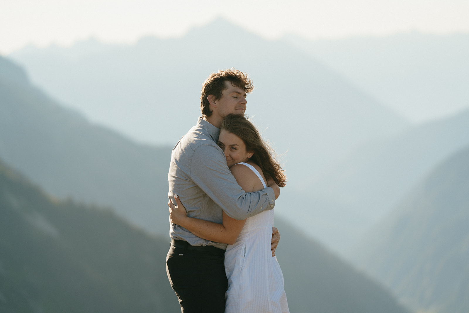 A couple embraces on a mountain peak in Washington during their engagement session, surrounded by stunning alpine scenery.