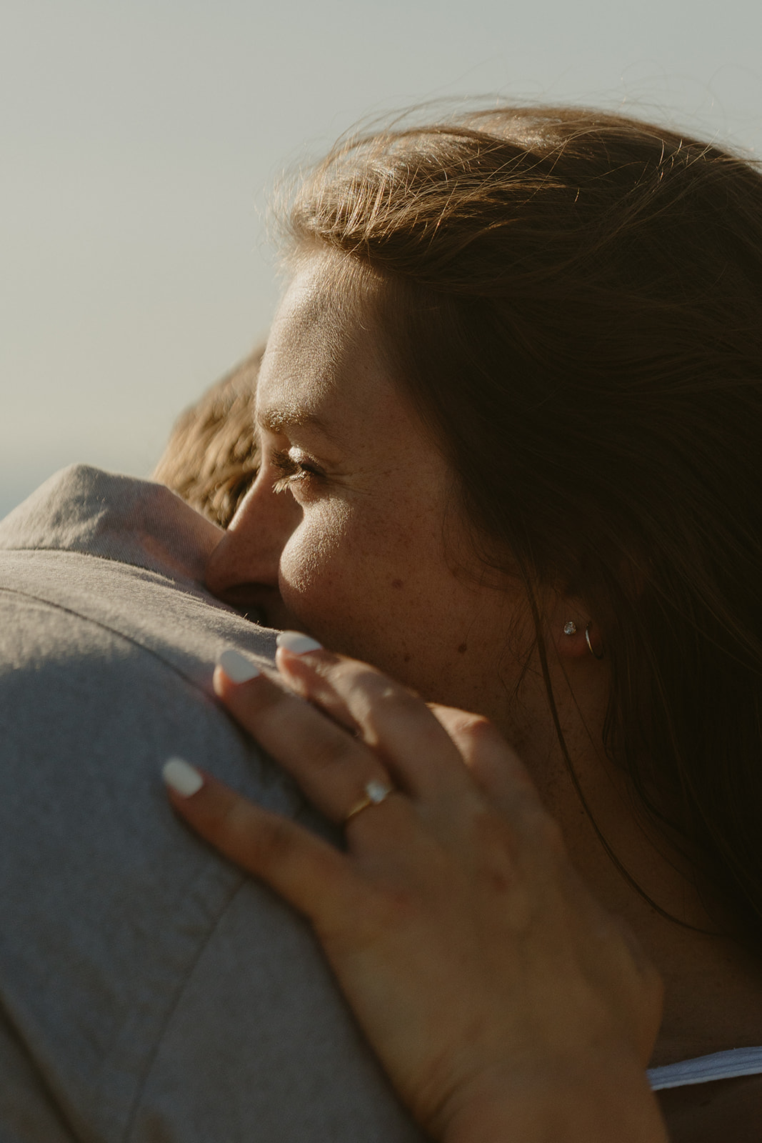 Close up of woman cuddling into man's shoulder while smiling and showcasing her engagement ring