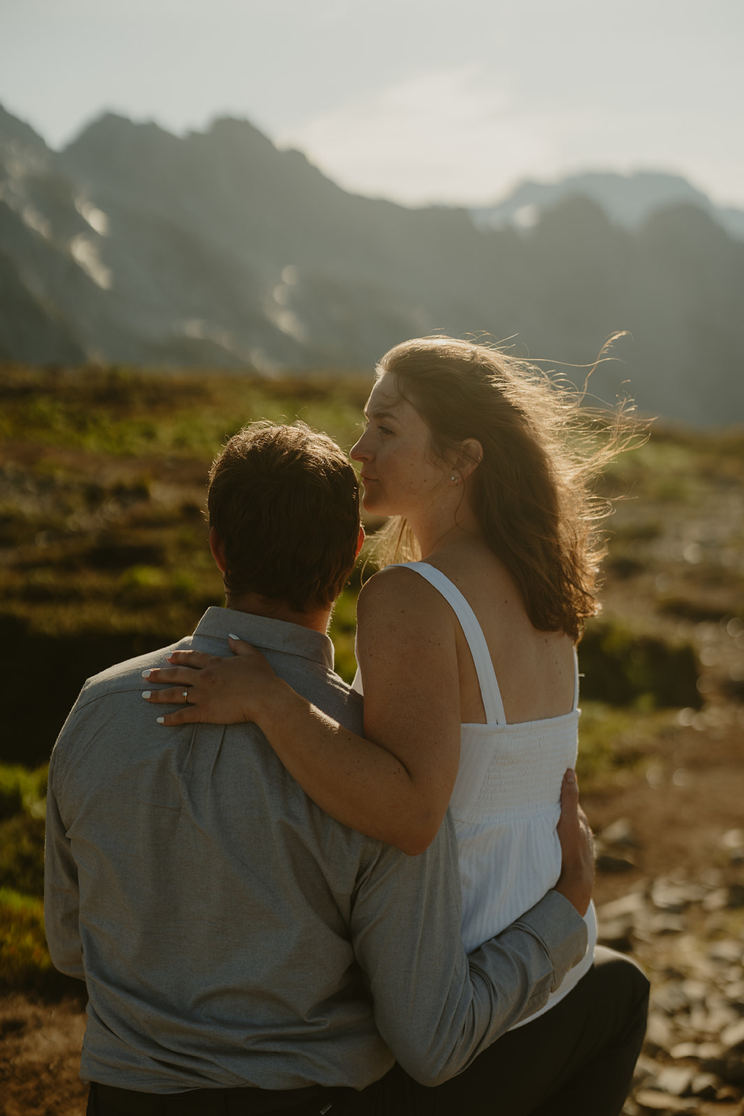 A couple embraces on a rocky mountain peak during their engagement session, surrounded by breathtaking scenic views.