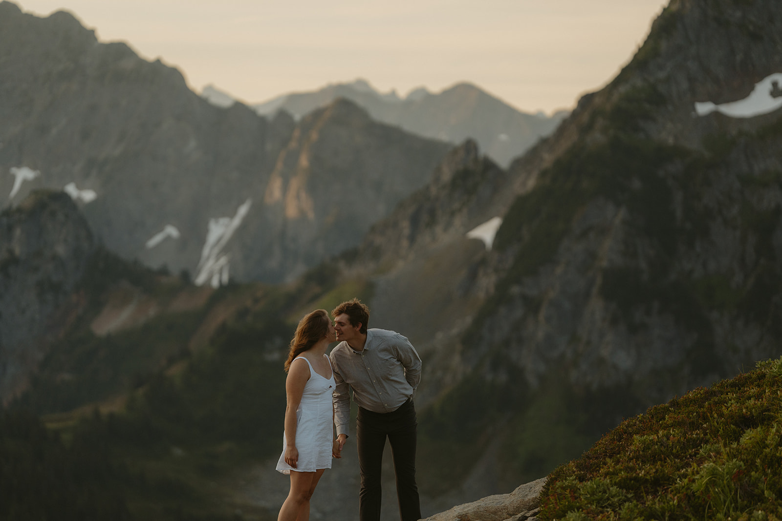 Couple stands in front of expansive view of Washington mountains while leaning together to kiss