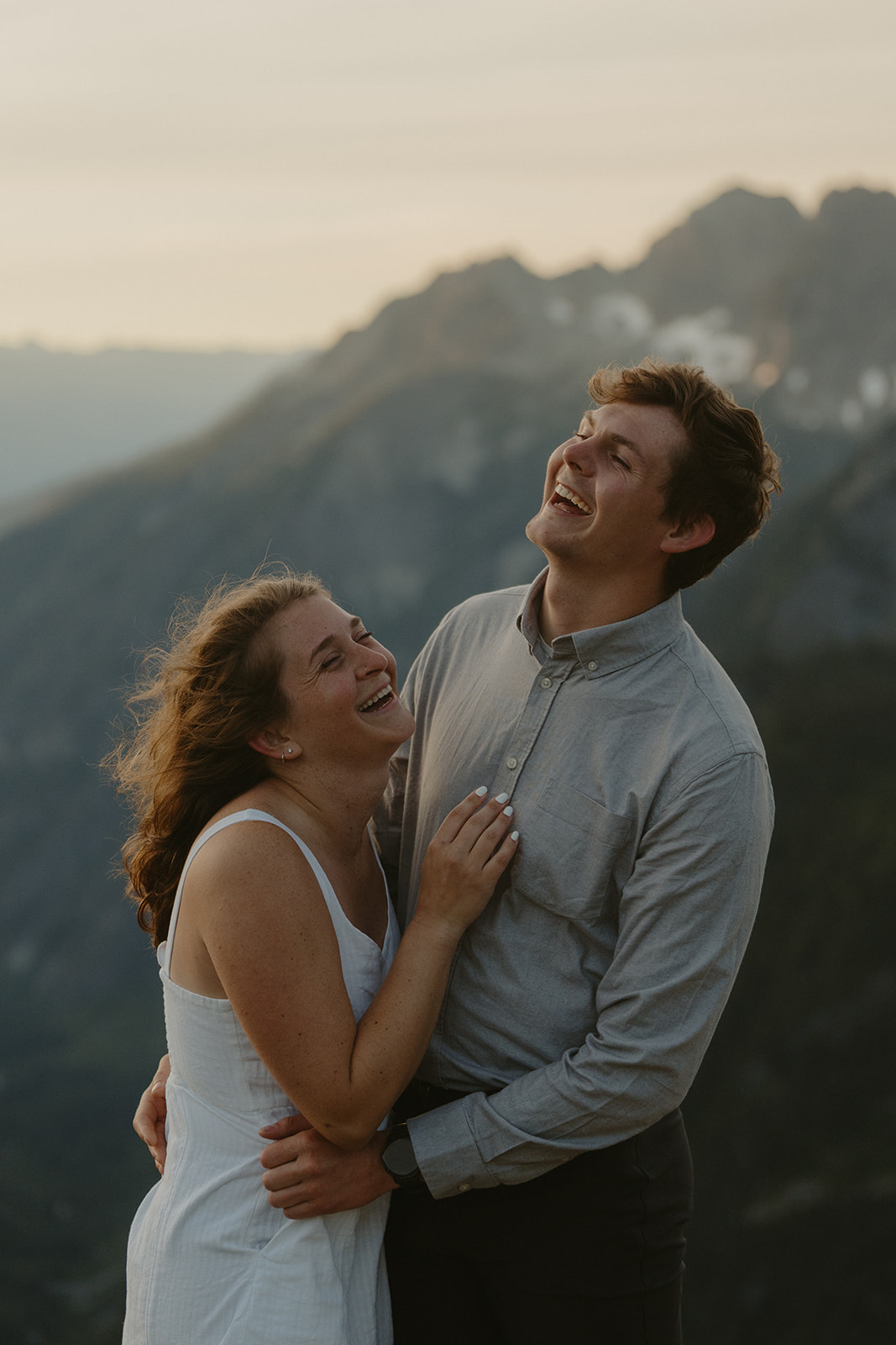 Close-up of a couple laughing together with mountains in the background, capturing the joyful essence of outdoor engagement photos.