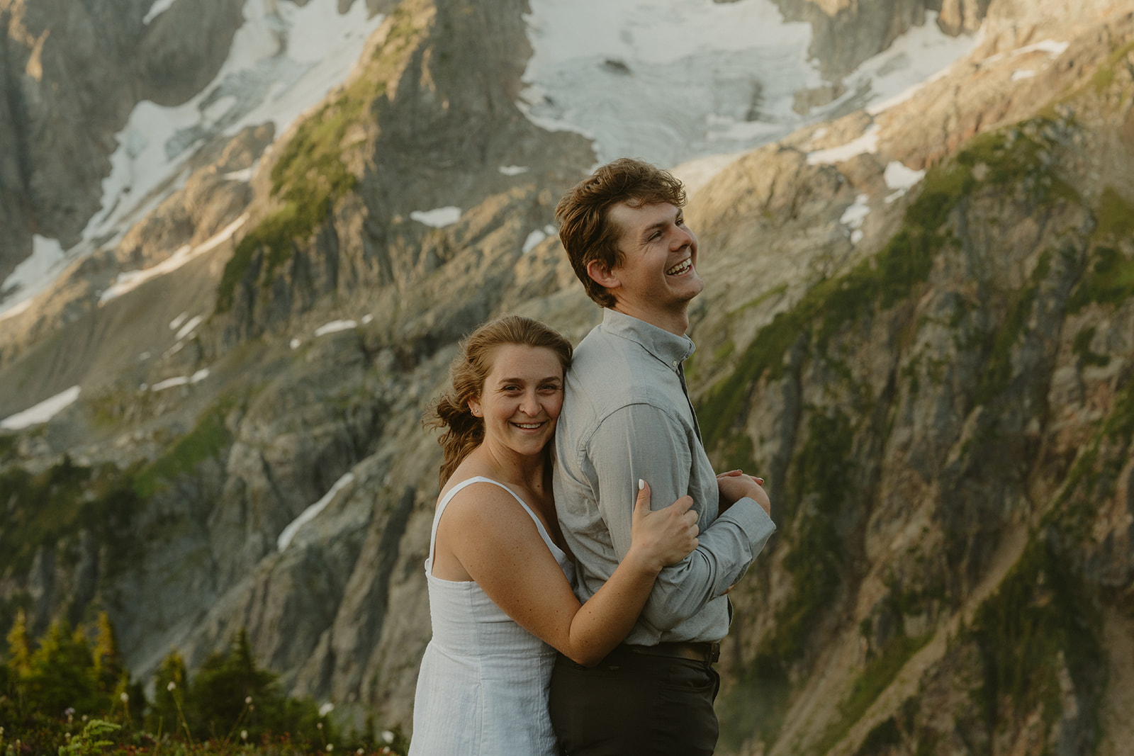 A couple embraces on a rocky mountain peak during their engagement session, surrounded by breathtaking scenic views.
