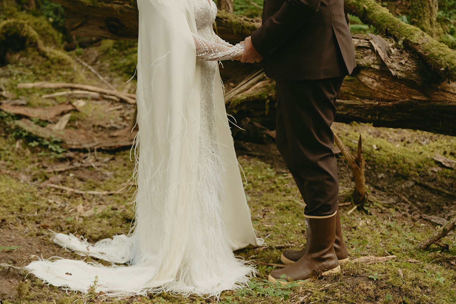 Close up of bride and groom holding hands while bride wears long flowing wedding gown, and groom wears brown suit with brown rain boots