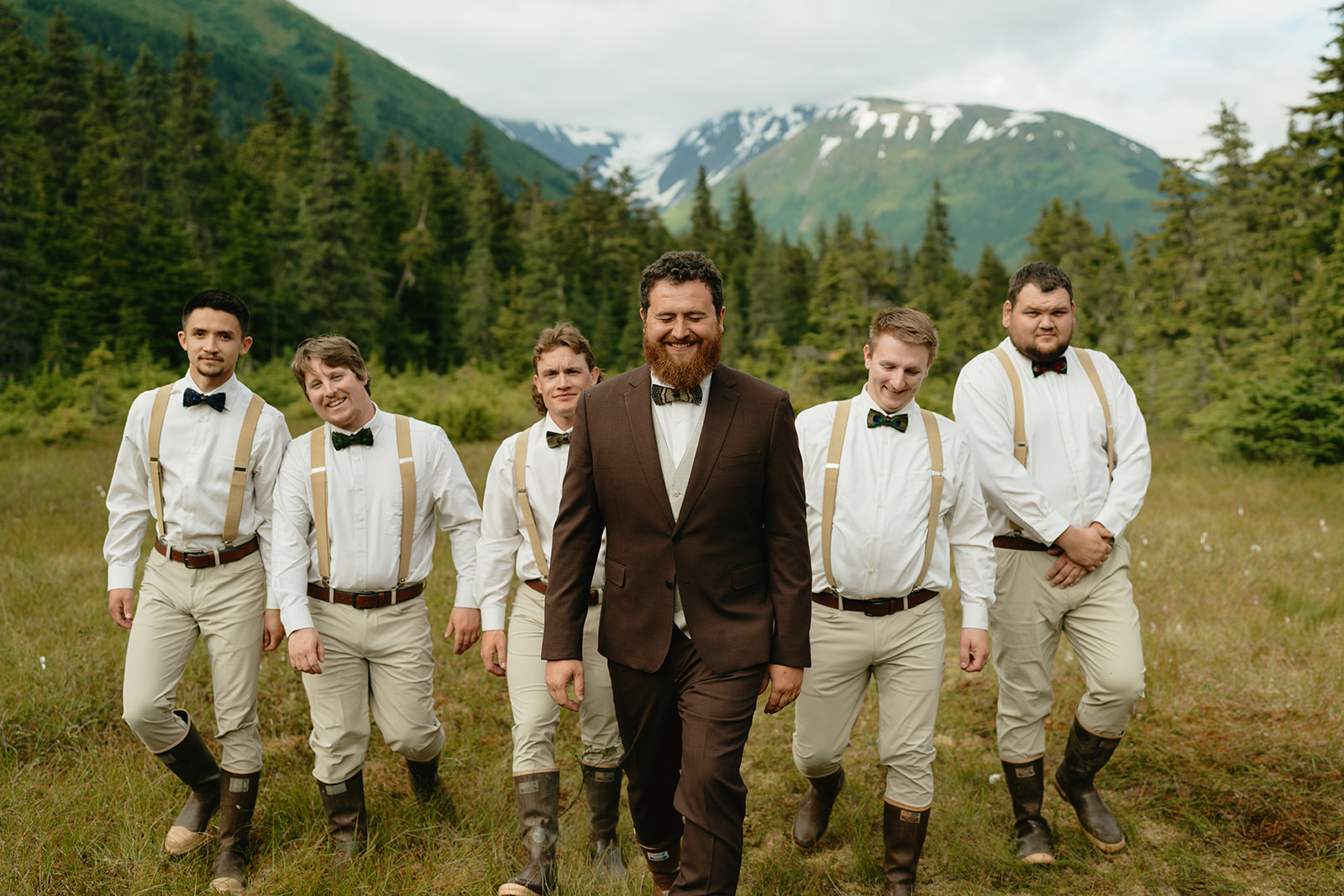 Groom walks with groomsmen walking behind him in a line all laughing and having fun together.