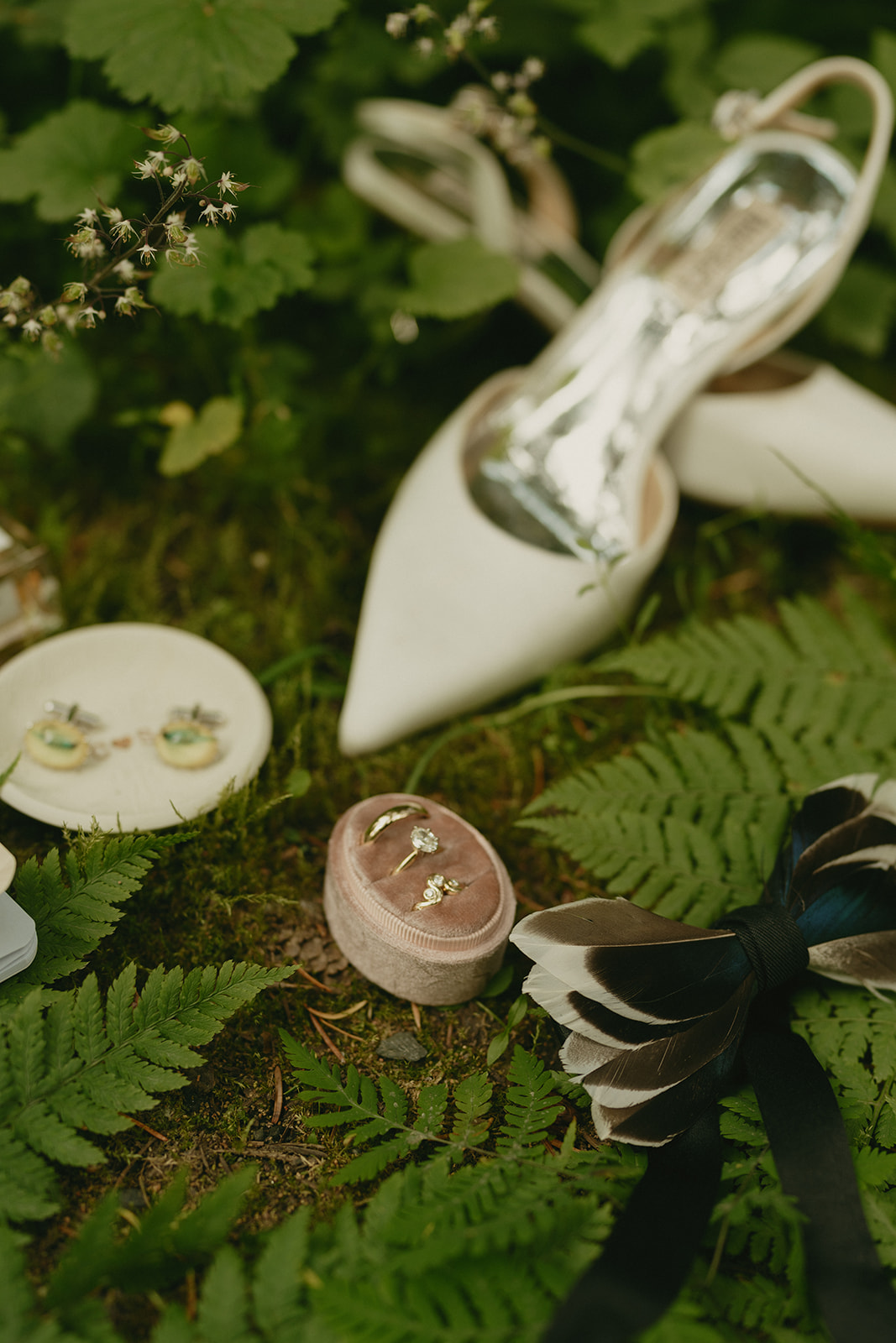Bridal accessories with shoes, bow and earrings laying on forest floor with greenery around it before couples eloping to Alaska.