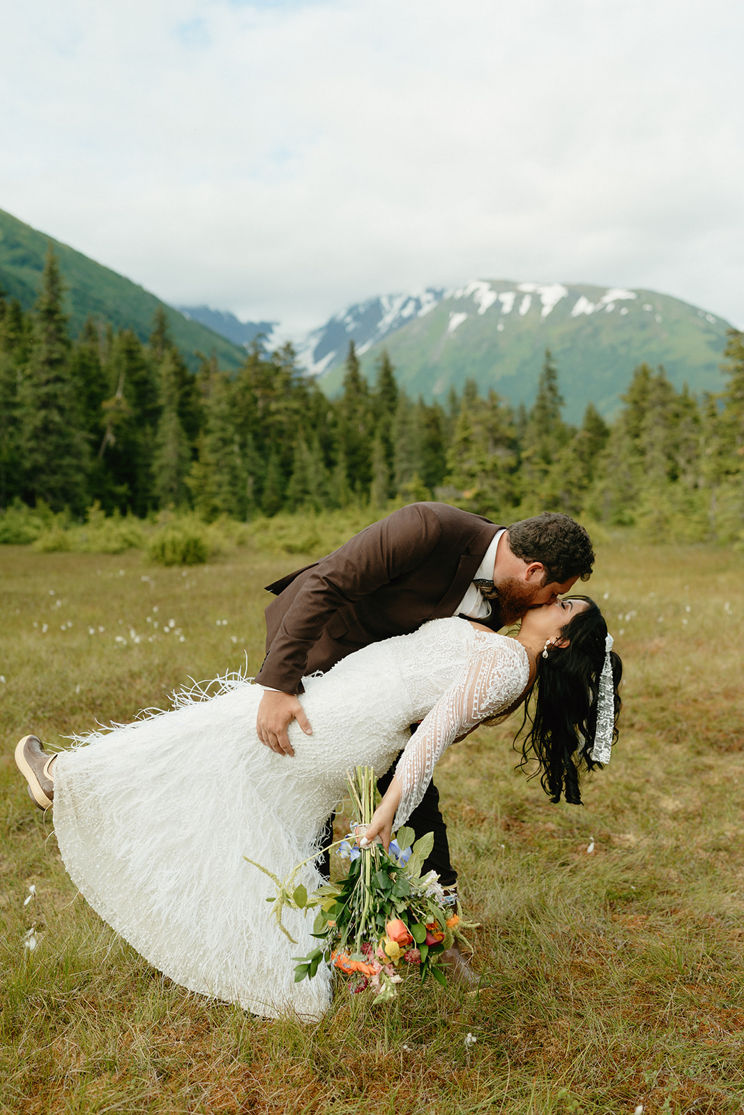 Groom dips bride for a dramatic kiss in front of beautiful Alaska mountains after eloping to Alaska.