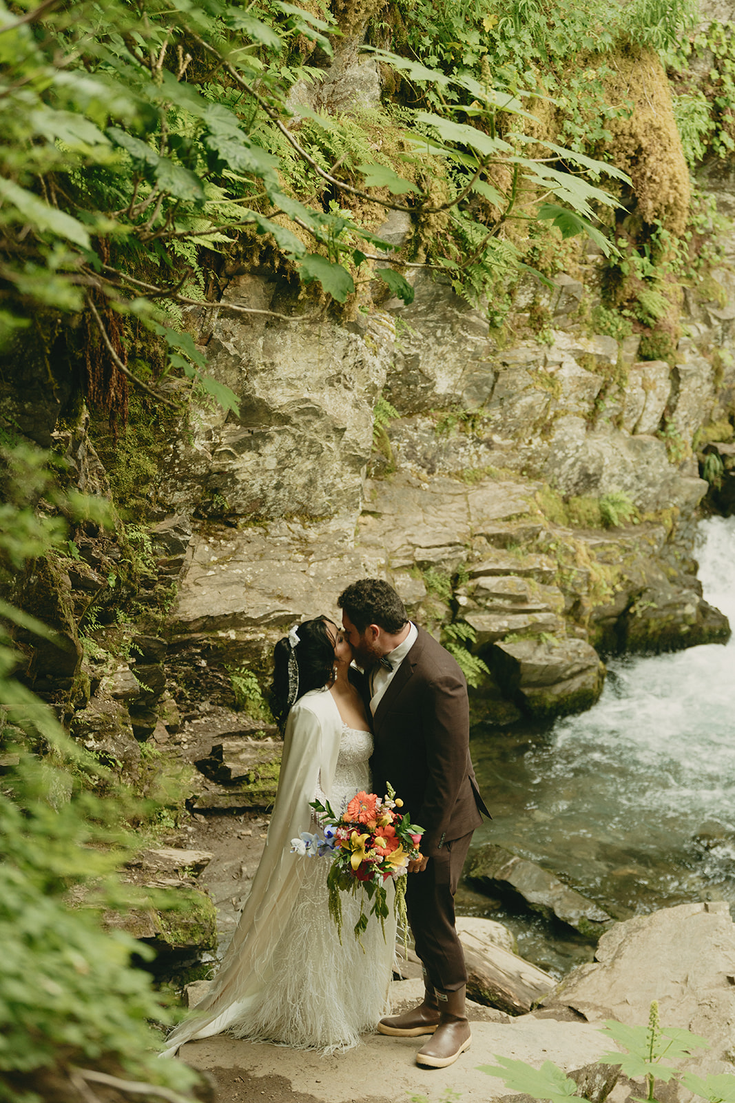 Bride and groom kiss in front of waterfall after eloping to Alaska