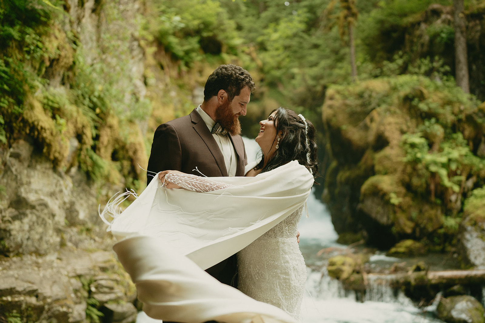 Bride swings her cape around in front of her and groom while she smiles and looks up at him.