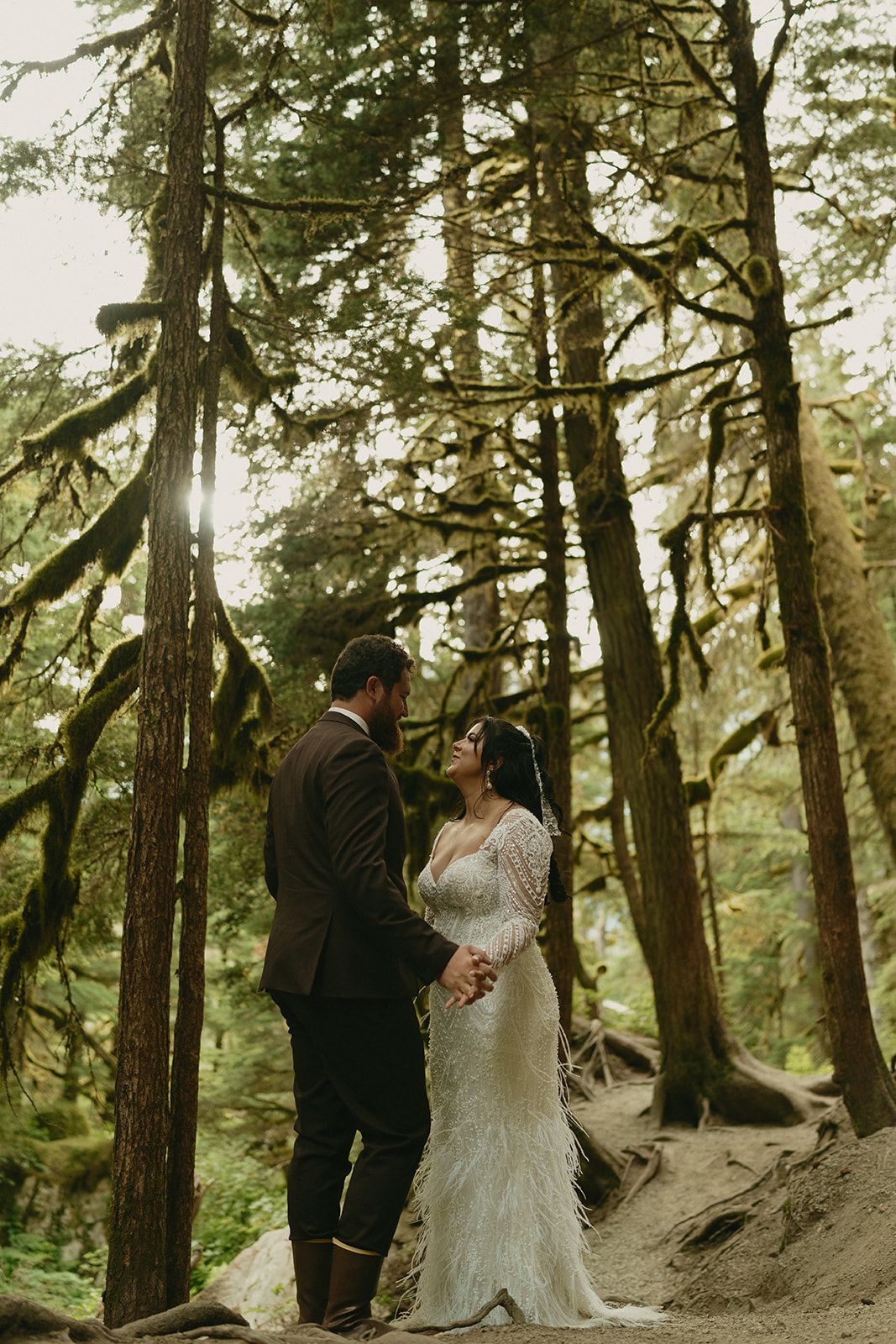 Bride and groom standing together amidst tall trees in forest after eloping to Alaska.