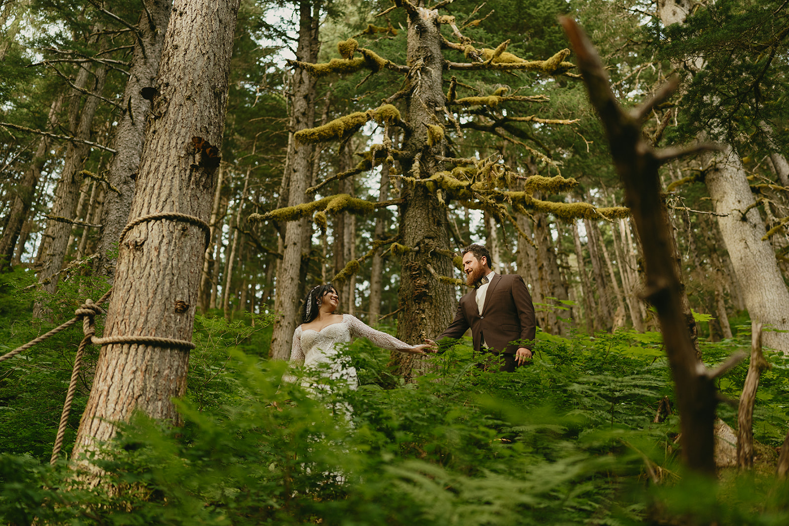 Bride and groom walking through forest in Alaska holding hands after their elopement ceremony.