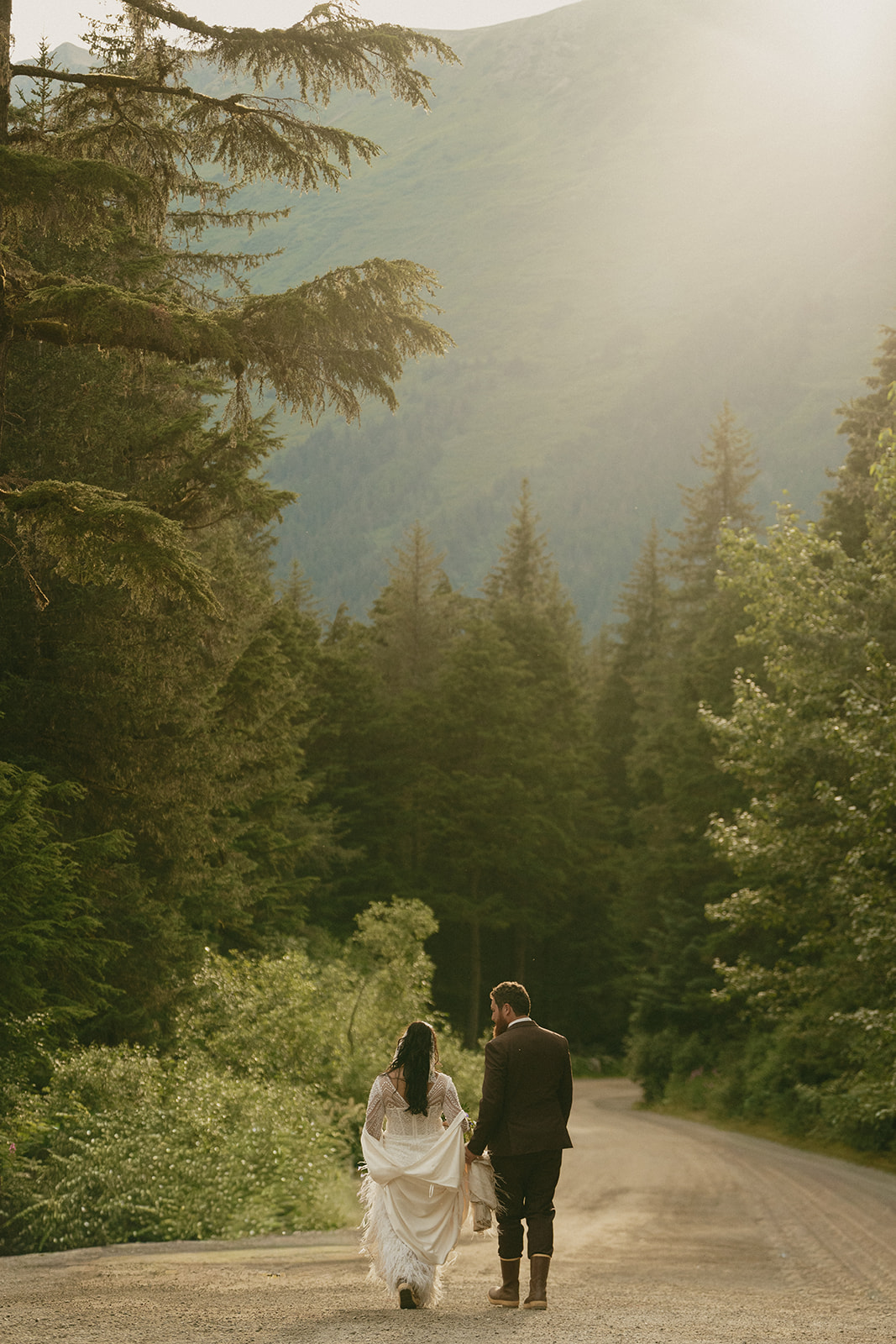 Bride and groom walk down trail together after eloping to Alaska being surrounded by incredible natural beauty.