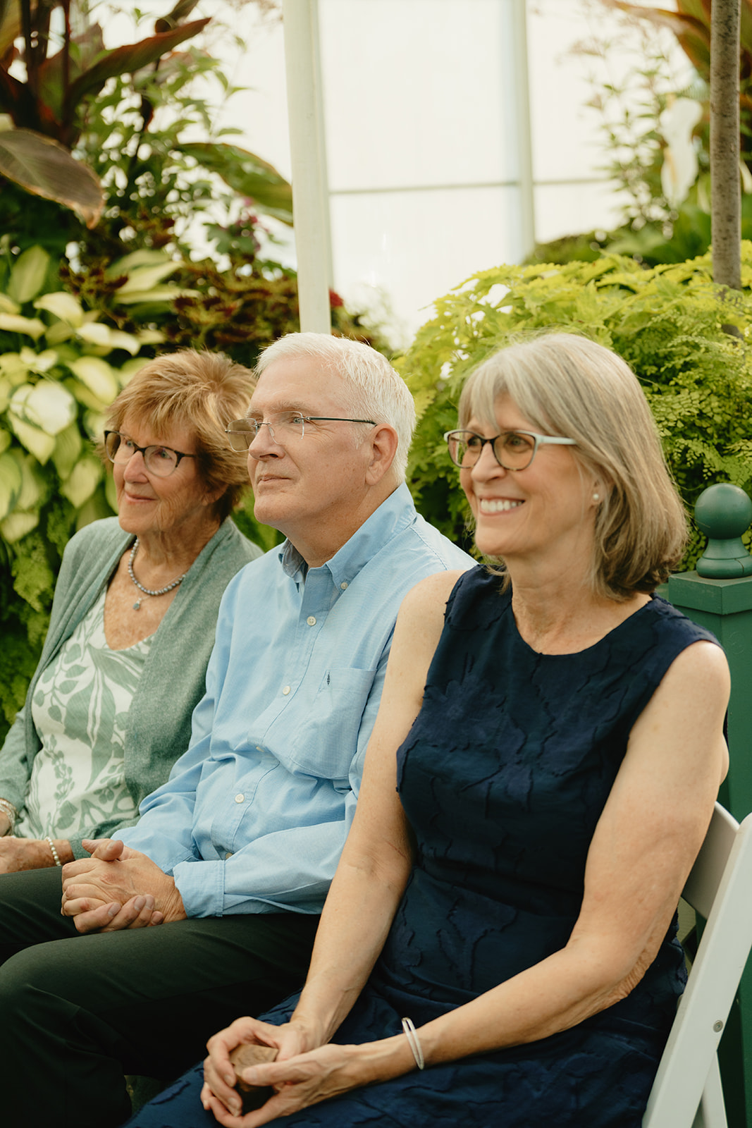 Guests seated among plants inside the greenhouse, smiling during a heartfelt wedding ceremony