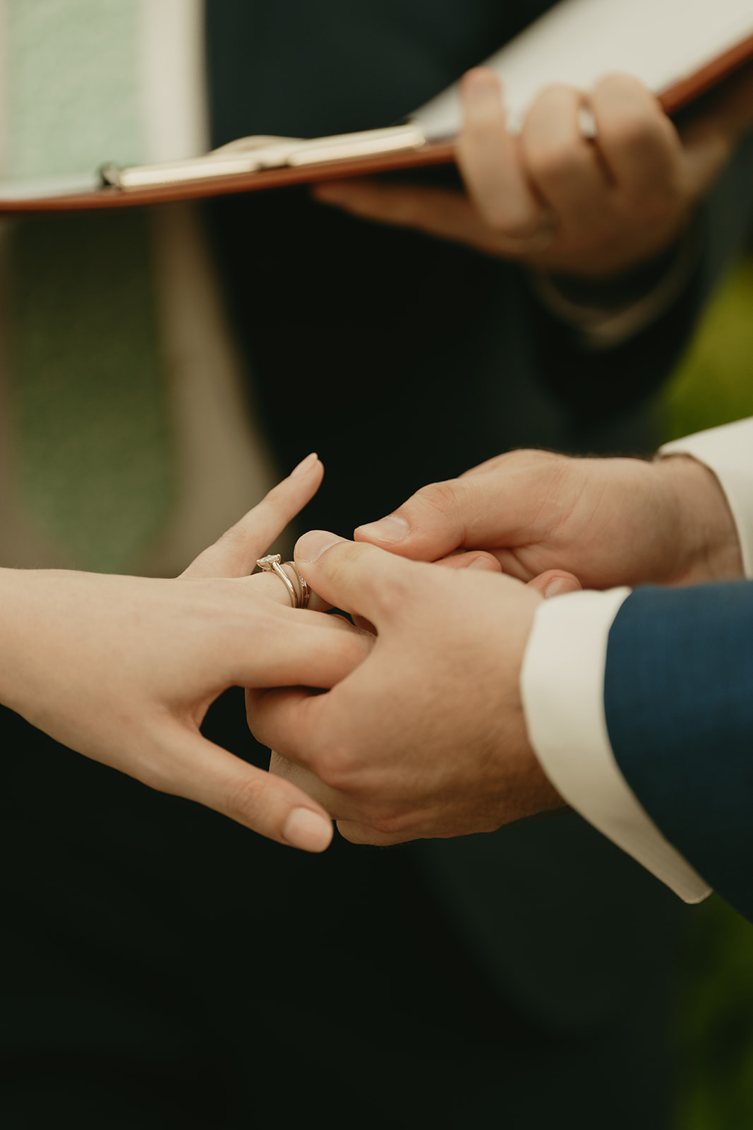Close-up of the groom placing the wedding ring on the bride’s hand, during a tender moment at their greenhouse wedding.