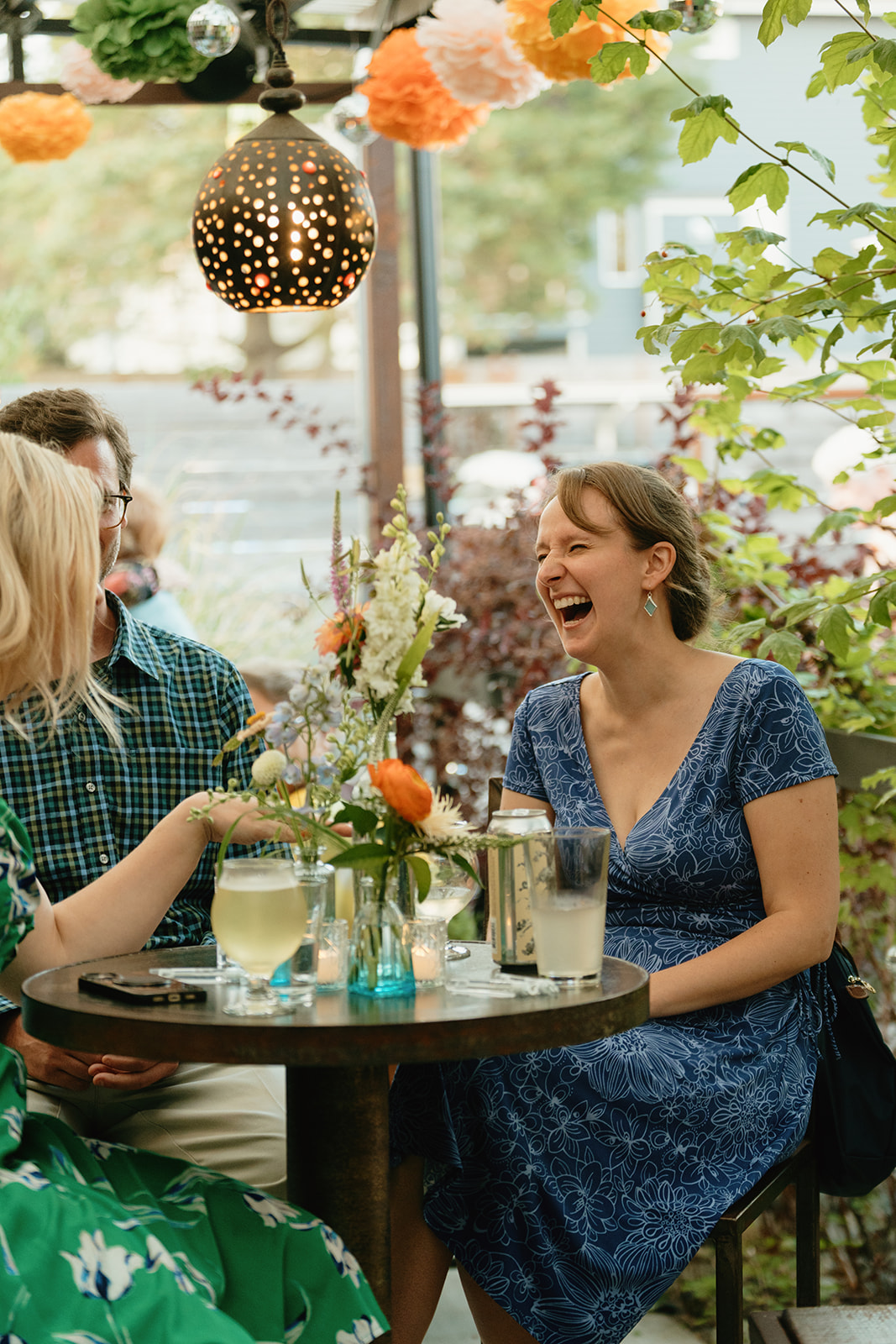 Wedding guests share laughter and wine at an intimate outdoor reception table, decorated with fresh flowers and candlelight.