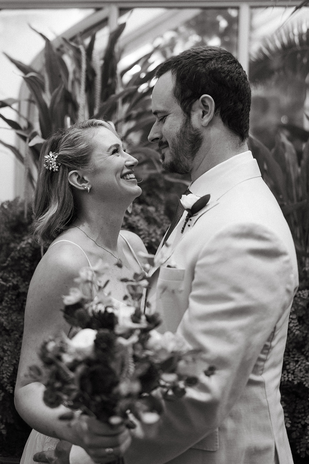 Black and white portrait of the couple holding each other and smiling during their heartfelt greenhouse wedding.