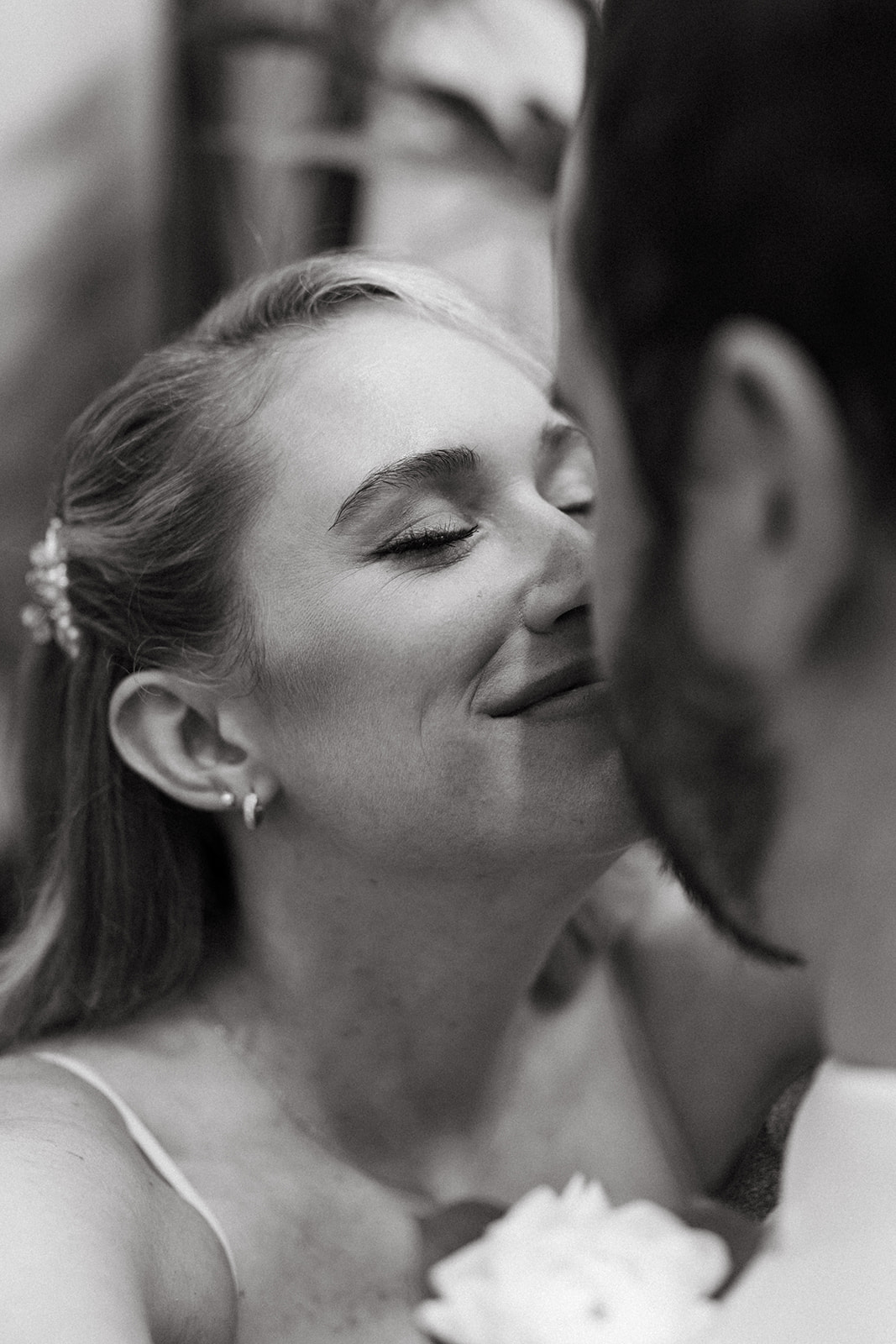 Black and white close-up of bride smiling softly with her eyes closed as she leans in toward her partner during a greenhouse wedding.