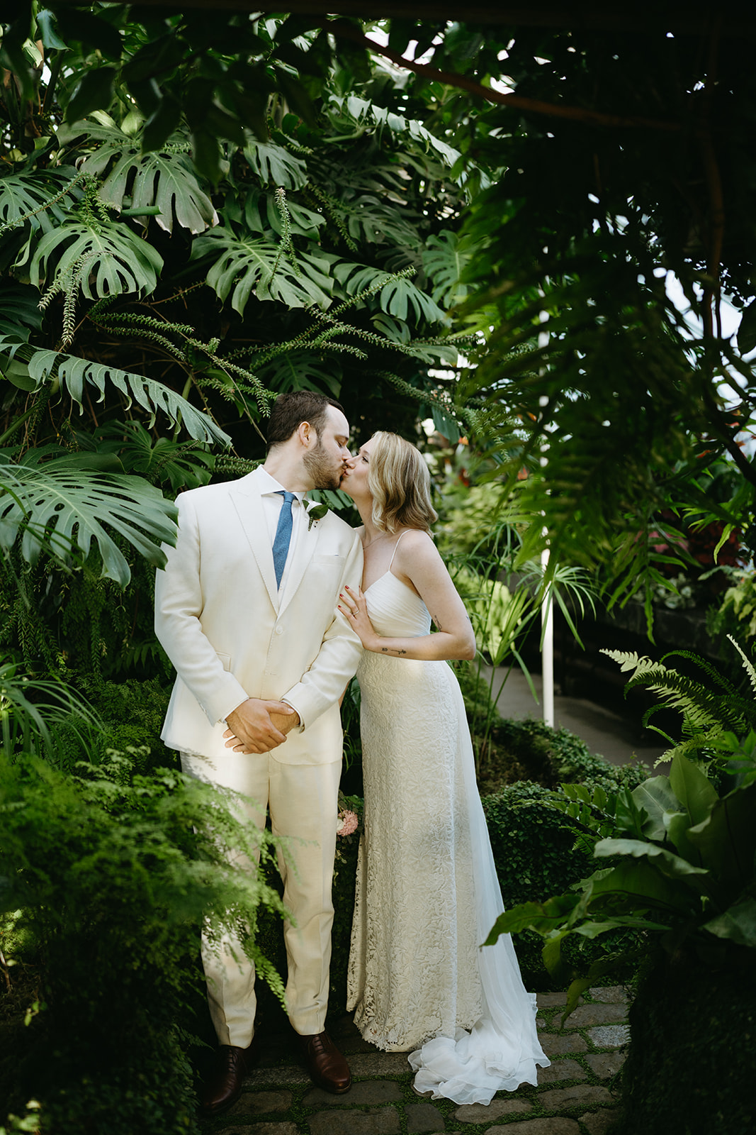 Newlyweds share a kiss surrounded by lush jungle-like greenery inside a dreamy wedding venue in Washington.