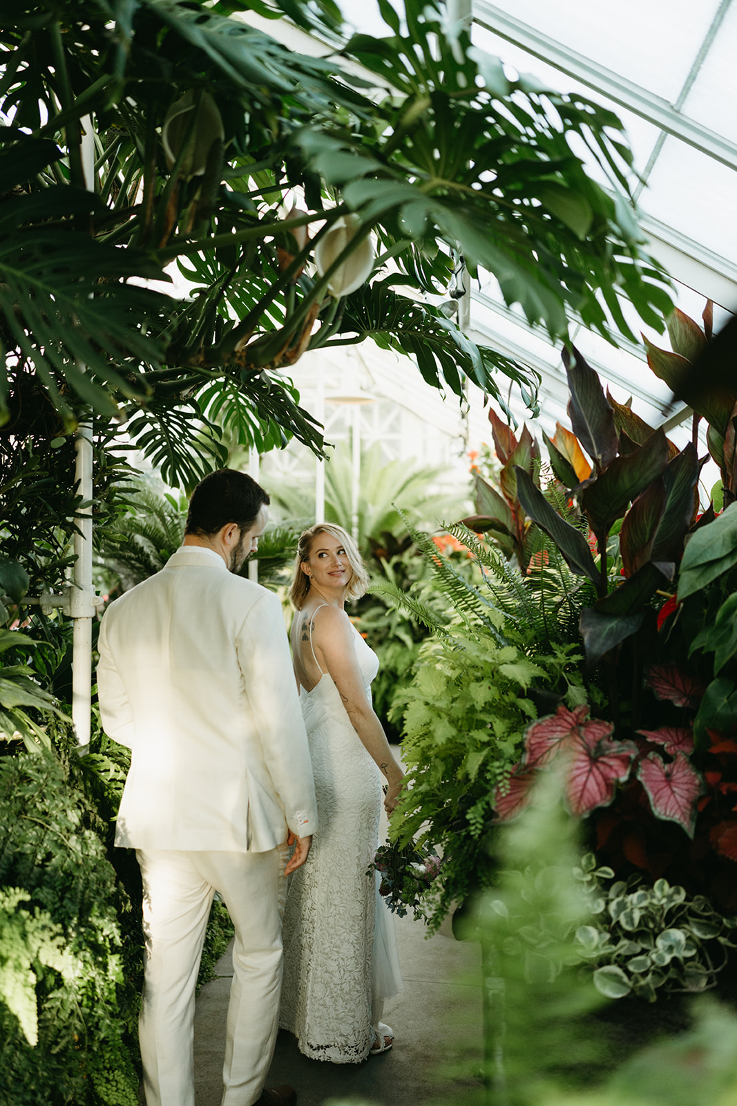 Newlyweds explore a glasshouse filled with tropical greenery after their vows at a wedding venue in Washington.