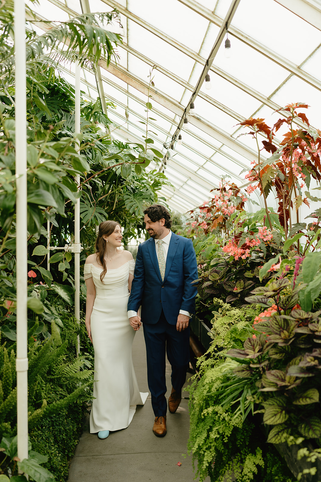 Couple walking through a lush indoor garden path during their romantic greenhouse wedding, surrounded by vibrant greenery.