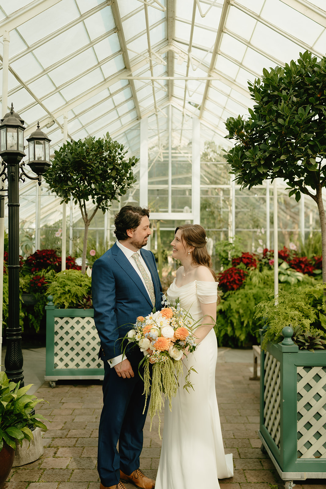 Joyful couple stands together inside a bright greenhouse filled with ferns and summer florals.