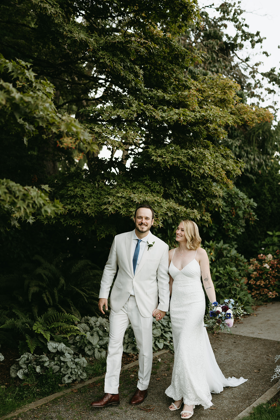 Couple walking along a garden path, hand in hand and smiling, moments after their intimate greenhouse wedding ceremony.