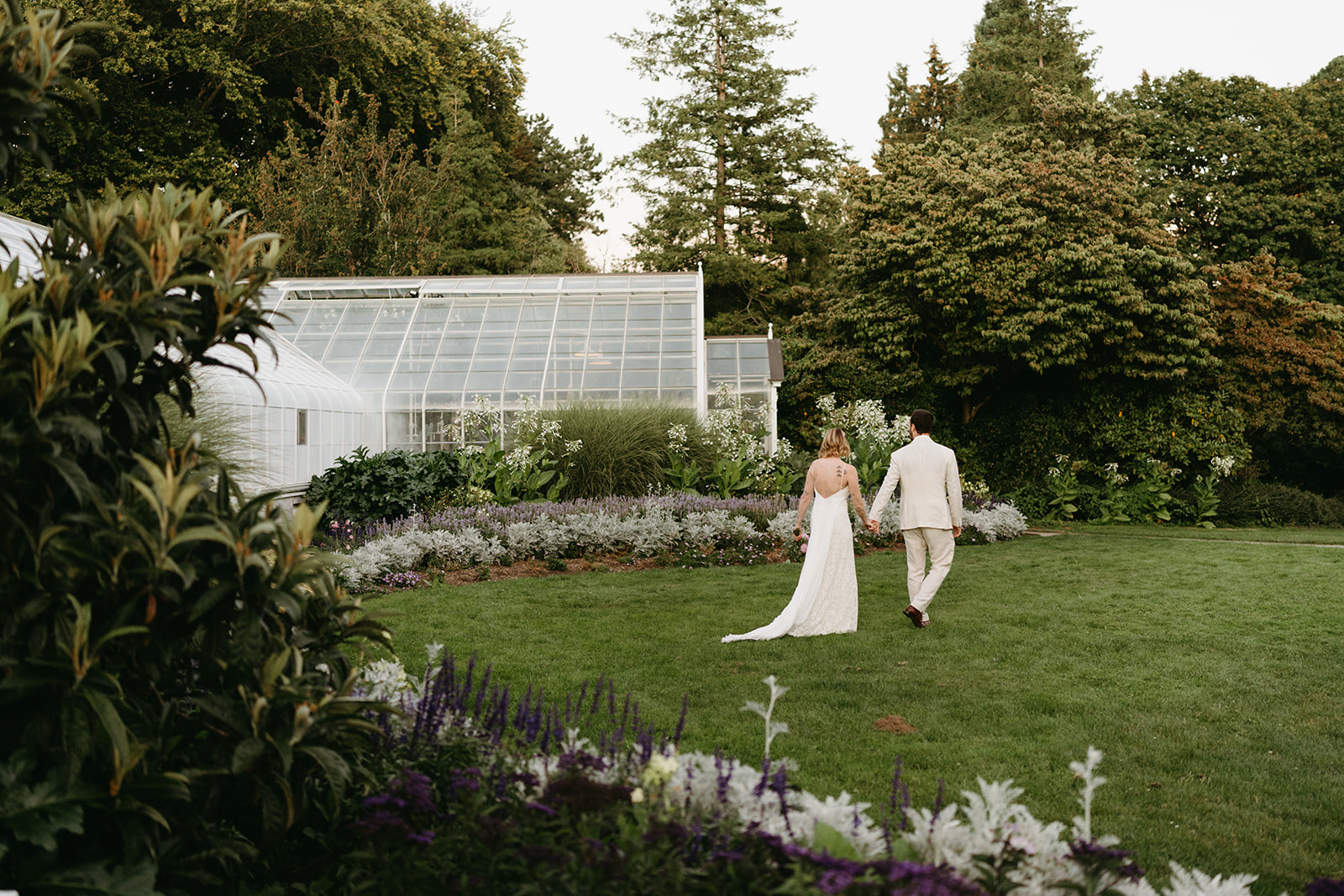 Couple walking toward a historic greenhouse surrounded by flowers at their serene wedding venue in Washington.