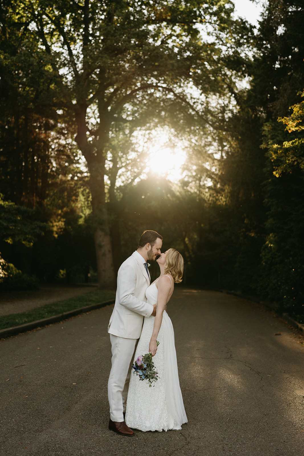 Groom gently kisses the bride’s forehead as golden light filters through the trees, capturing a quiet moment of connection.