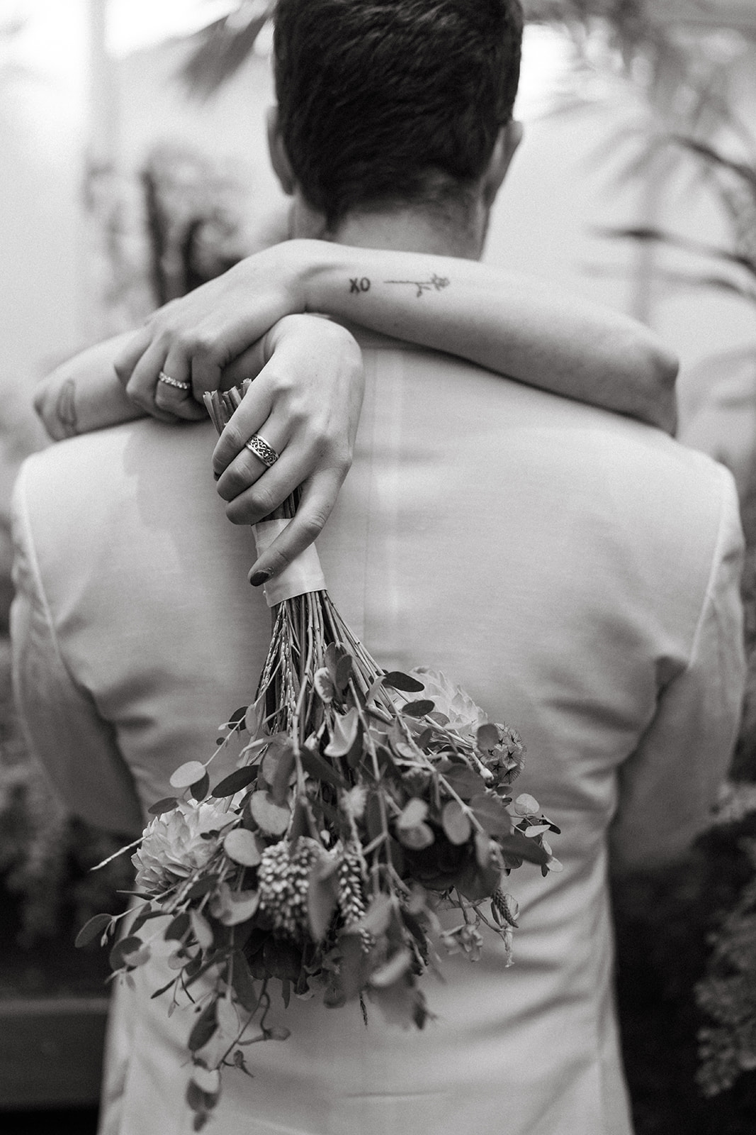 Intimate black and white photo of a bride hugging her partner, bouquet draped over his shoulder.