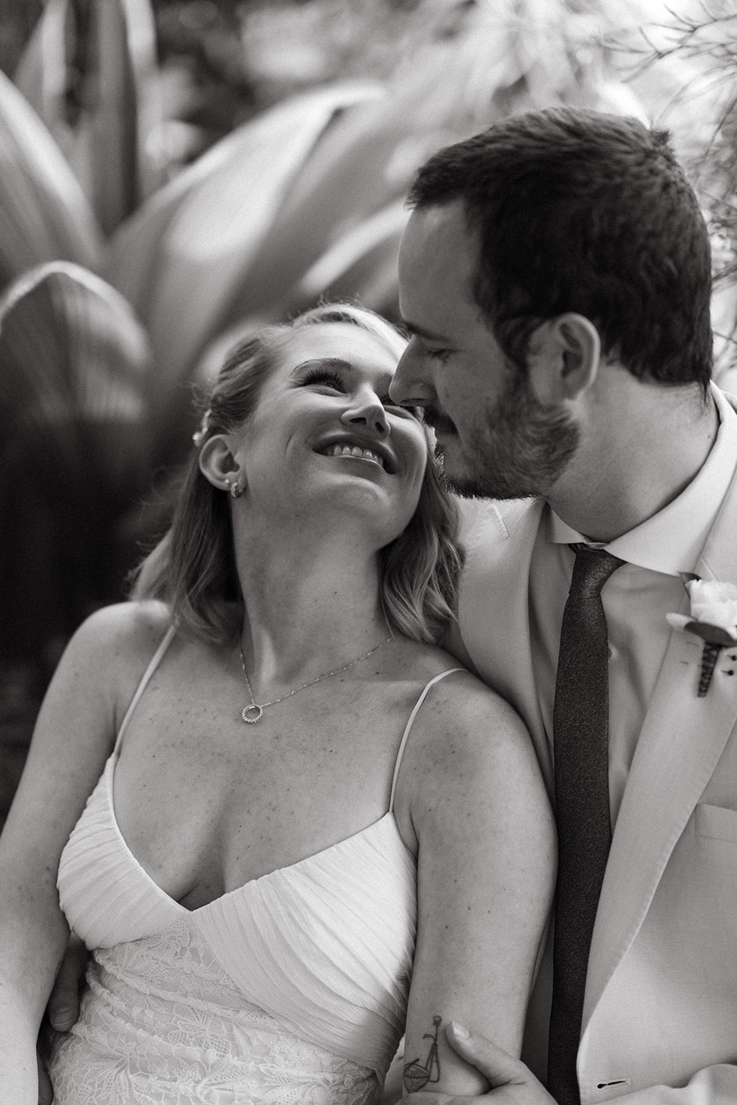 Black and white portrait of a couple smiling tenderly at each other, sharing a quiet, joyful moment after their greenhouse wedding.