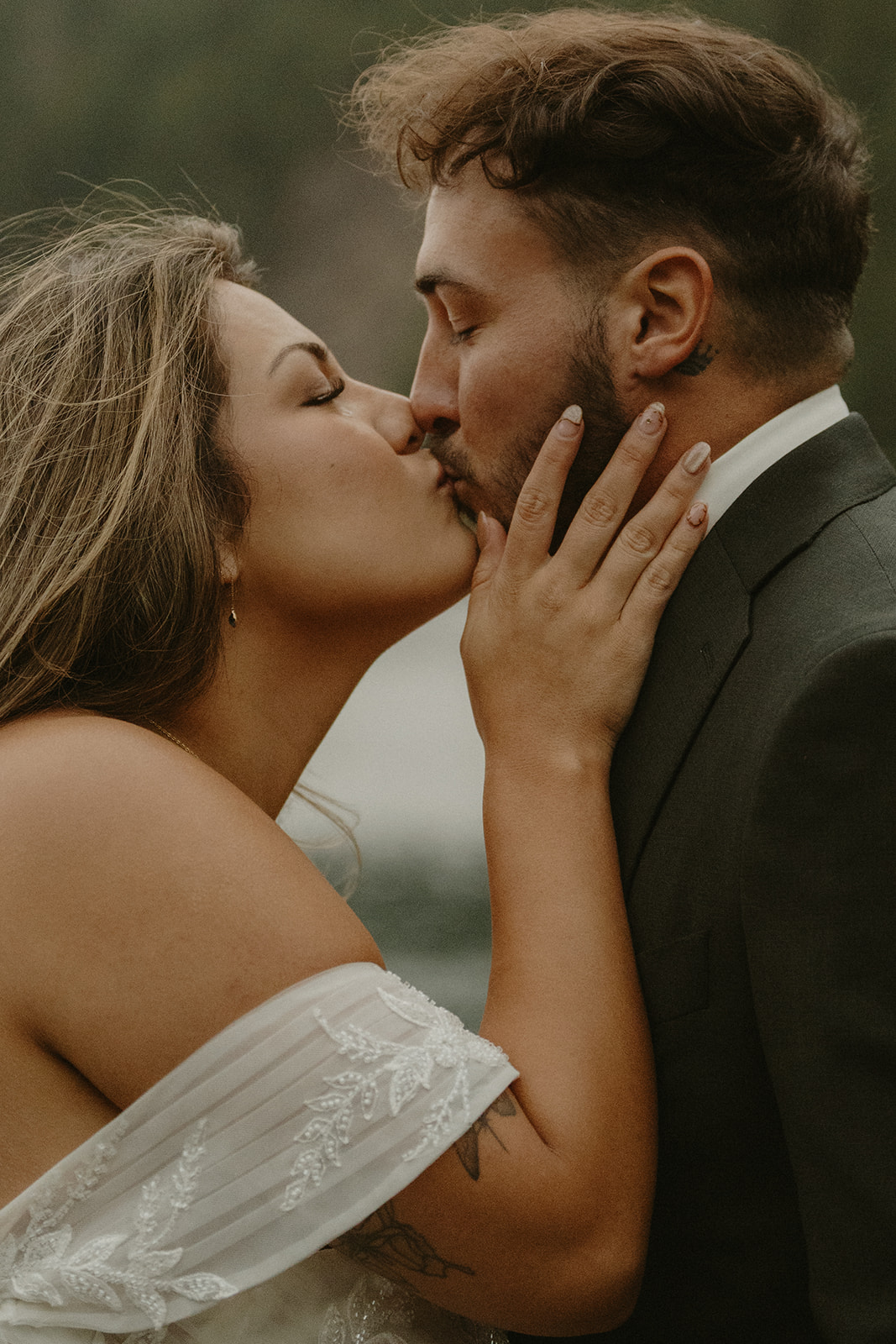 A close-up of the bride and groom sharing a soft, intimate kiss, framed by the natural tones of the surrounding wilderness.