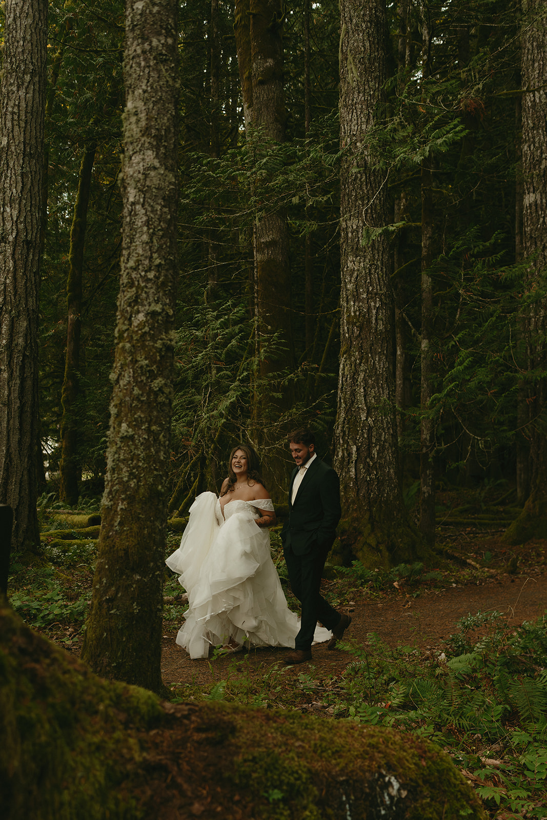 The bride and groom walk through a lush, mossy forest trail, tucked away in the heart of Olympic National Park.