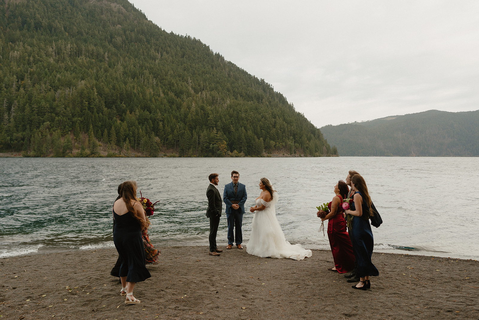 A small wedding ceremony takes place on the shore of a mountain lake, with the bride and groom joined by loved ones for their Olympic National Park elopement.
