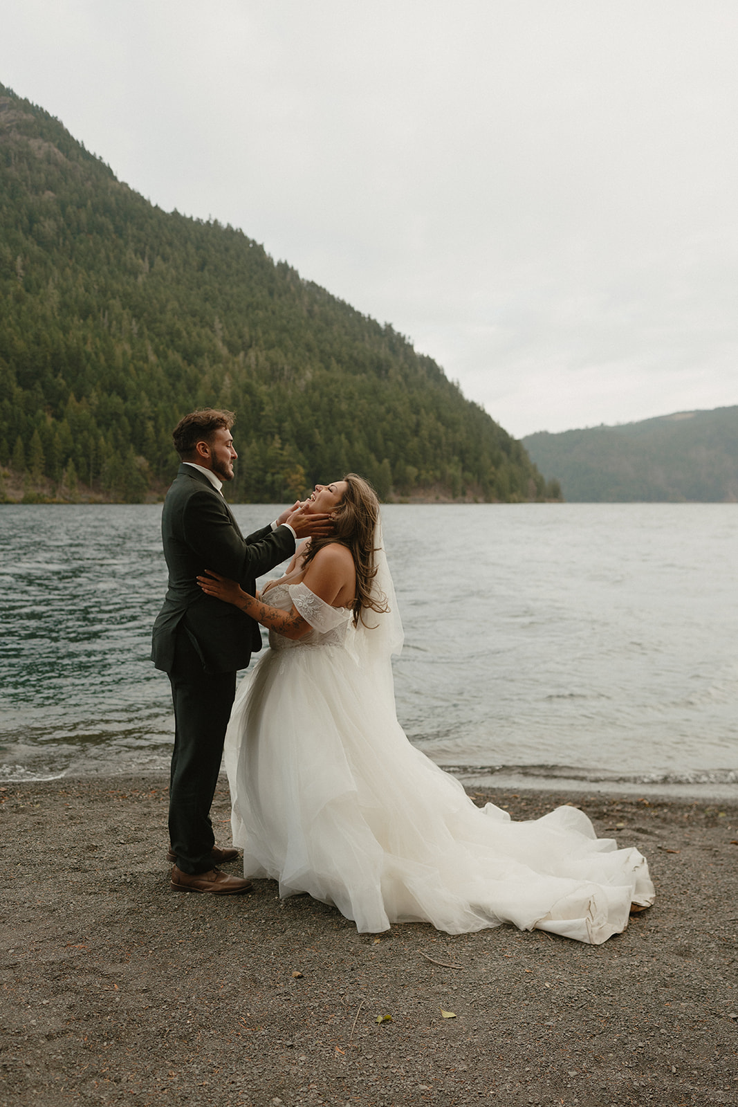 A candid moment between the bride and groom, smiling and holding each other by the lake during their Olympic National Park elopement.