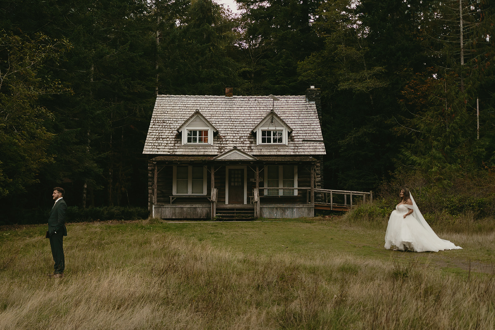 A bride approaches her partner for their first look in front of a historic cabin tucked into the forest, part of their Olympic National Park elopement.