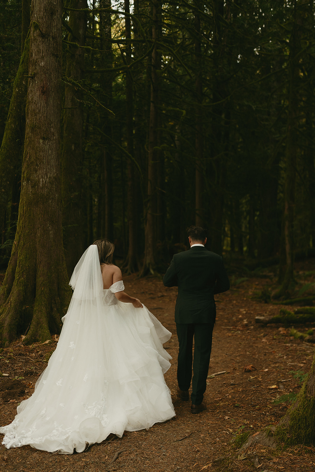 The bride and groom walk arm-in-arm along a fern-lined forest trail during their Olympic National Park elopement.