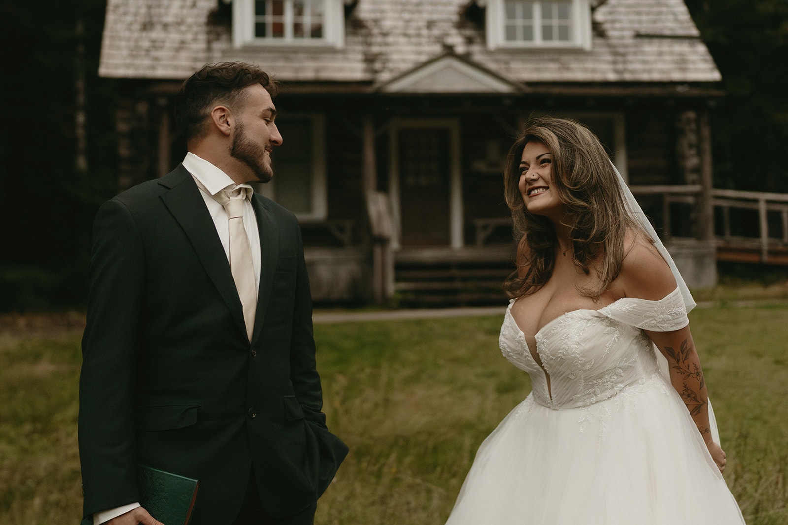 The bride and groom smile at each other warmly in front of a rustic wooden cabin, tucked away in the forest.