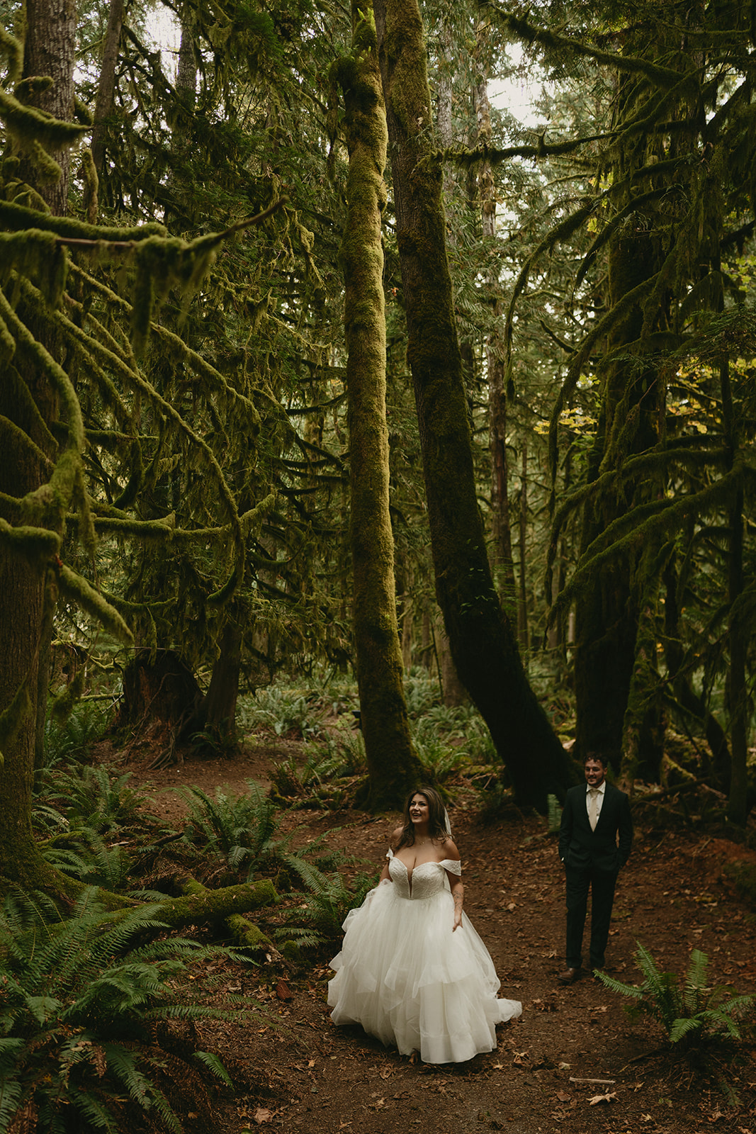 A bride and groom walk through an enchanting moss-covered forest, surrounded by towering old-growth trees during their Olympic National Park elopement.