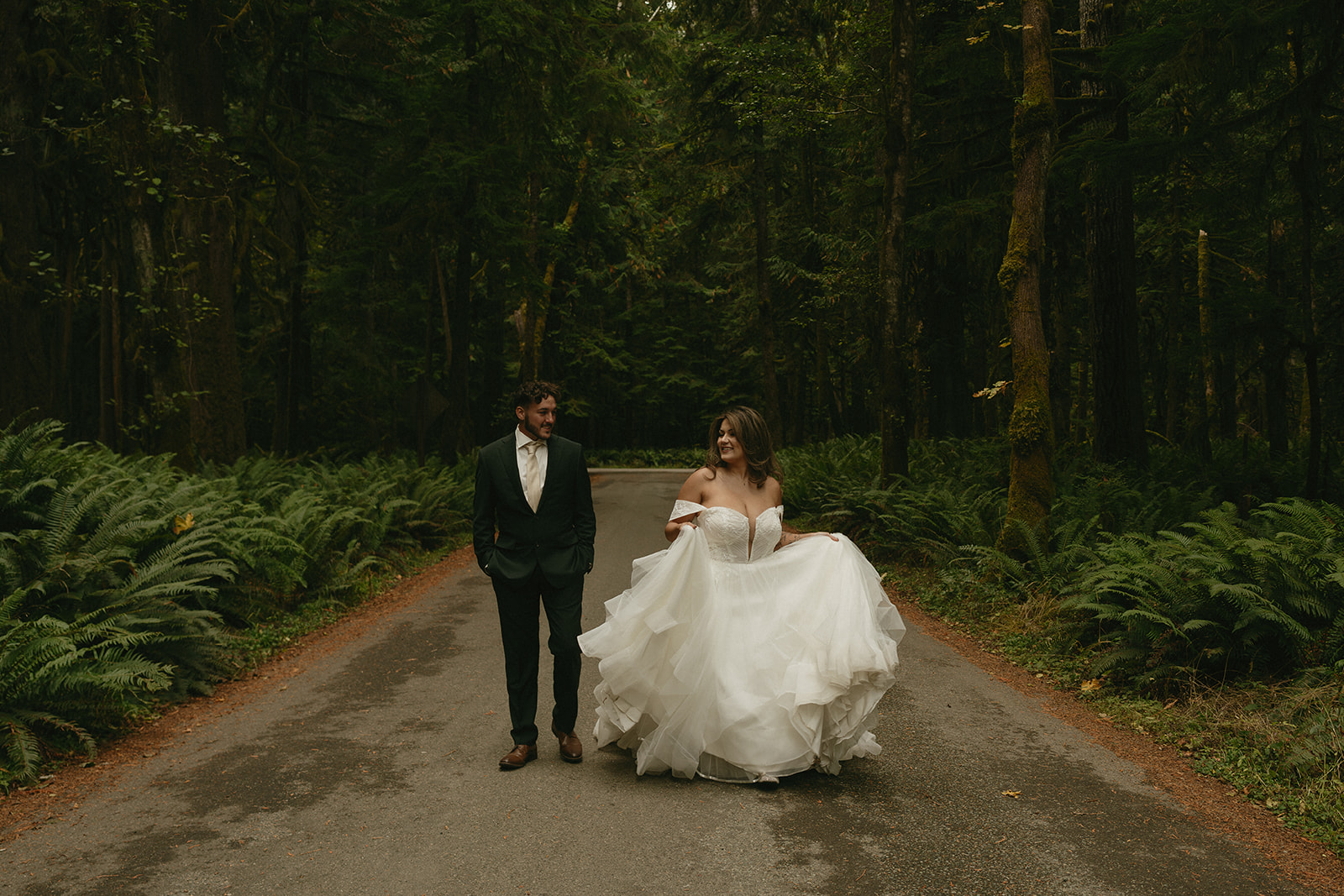 A close-up of the bride’s tattooed arm holding a vibrant bouquet of burgundy flowers, her lace gown soft against the green backdrop.