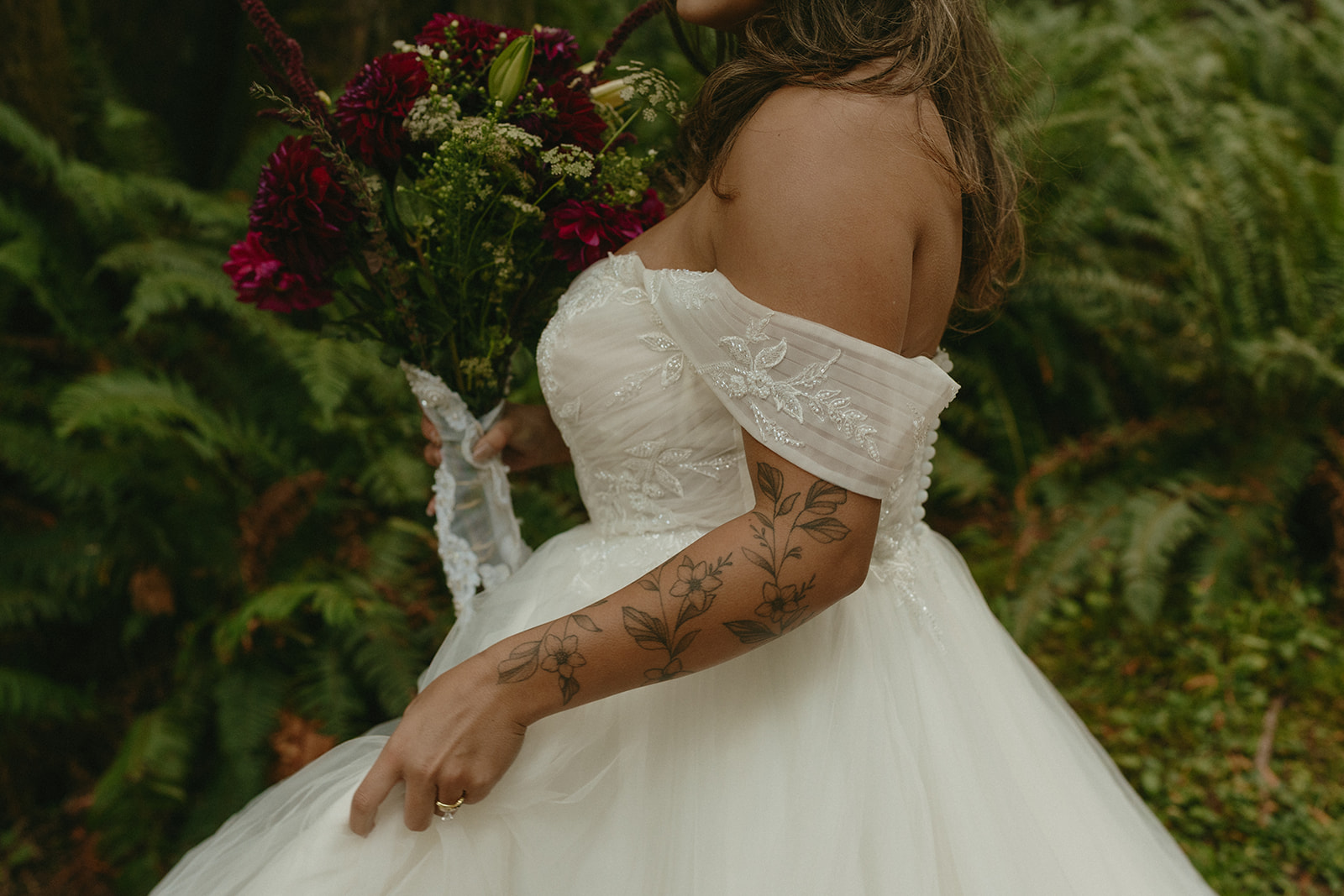 Framed by tall ferns and deep woods, the couple walks slowly down the center of a forest road, just the two of them.