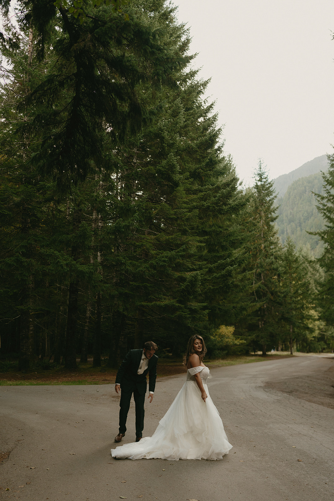 The couple pauses on a quiet road under a canopy of trees, sharing a moment of joy just after their ceremony.