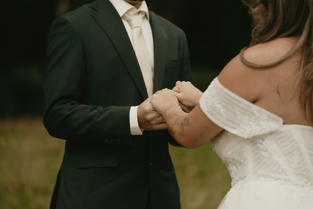Close-up of the couple holding hands, highlighting the bride’s tattoo and delicate lace wedding gown.
