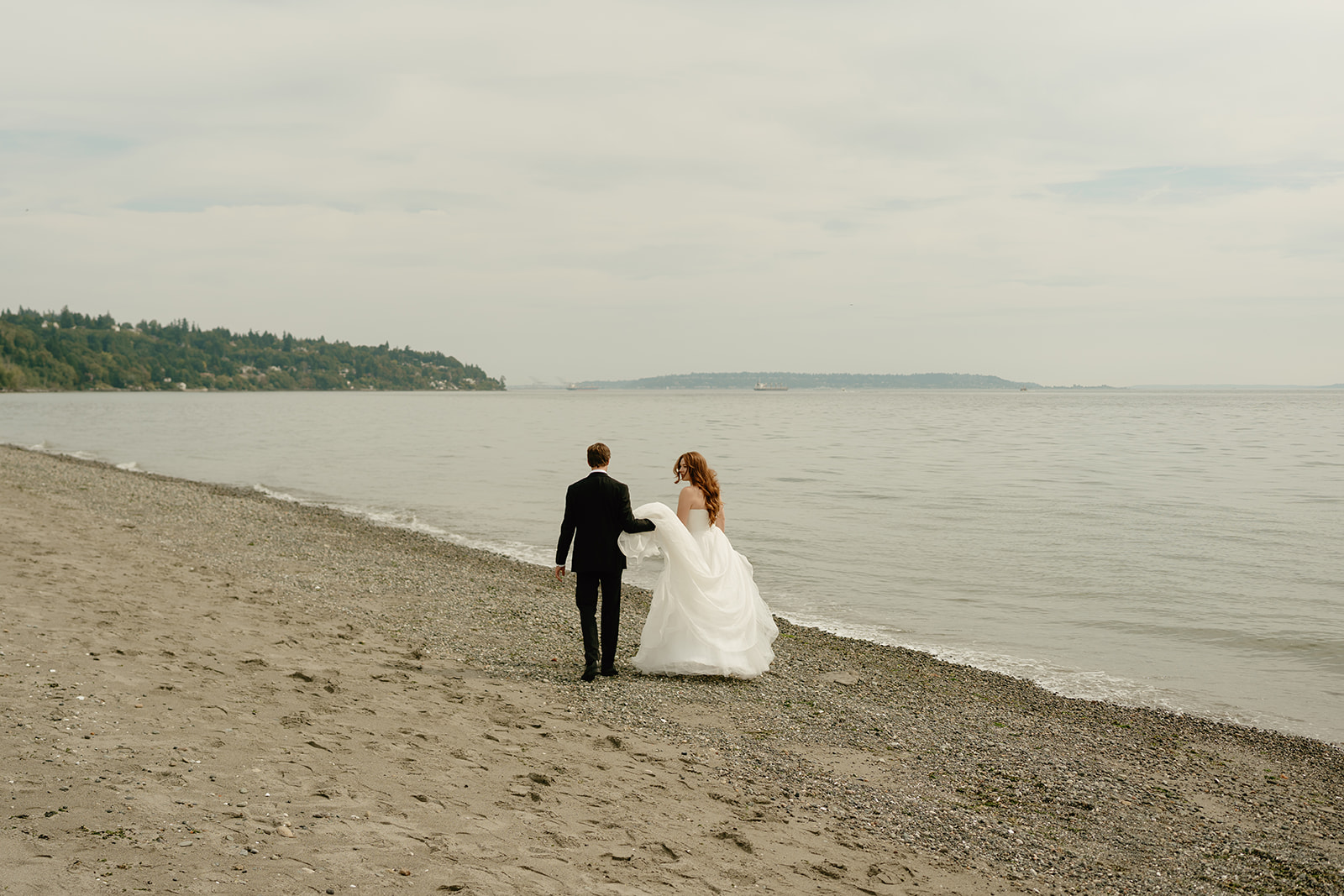 Bride and groom walk along a quiet Washington beach after their ceremony, the shoreline stretching peacefully beside them.