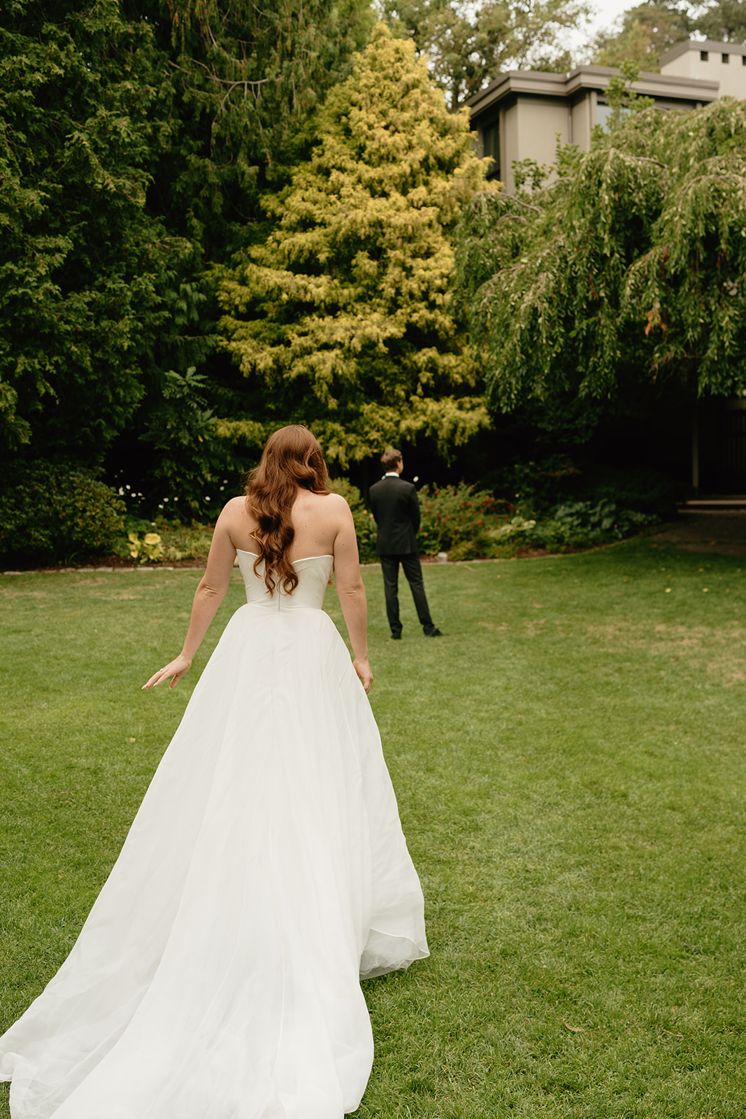Bride approaches her groom for a first look, framed by lush greenery in a serene garden setting.